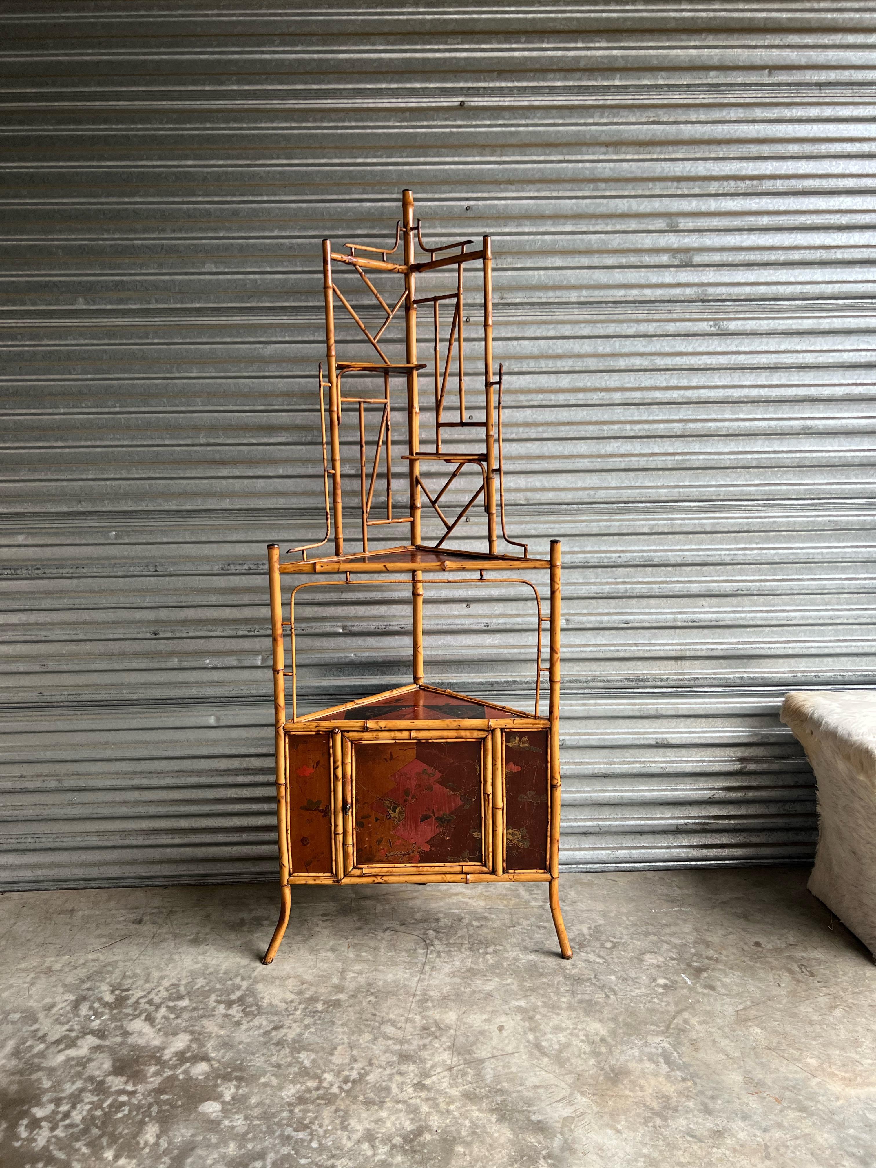 This is a late 19th century English bamboo corner cabinet. Its style is representative of the Aesthetic Movement that was in fashion during this era. The lacquered panels are russet and black and have leaves and other natural elements painted on