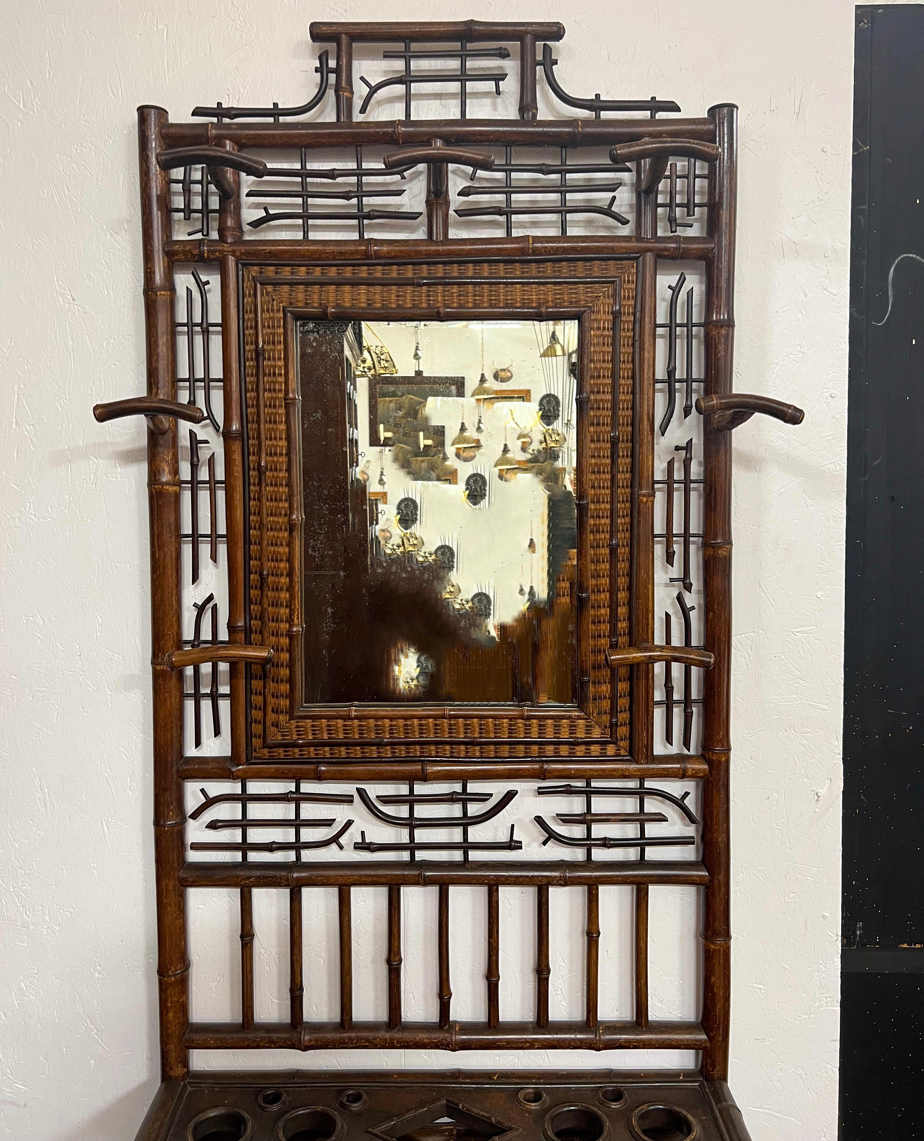 This is a 19th century burnt bamboo English hall tree. It has quite a few hooks for coats and hats , but also includes spaces for umbrellas! This one is in particularly good condition. The mirror does show wear but is without cracks.