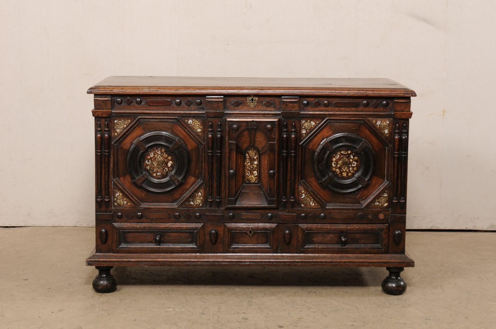 An English carved oak trunk with bottom drawer, circa 1820-50's. This antique trunk from England features an exquisitely hand-carved front facade with geometric shaped panels, and adorn with column, diamond, oval and round medallion accents, with an