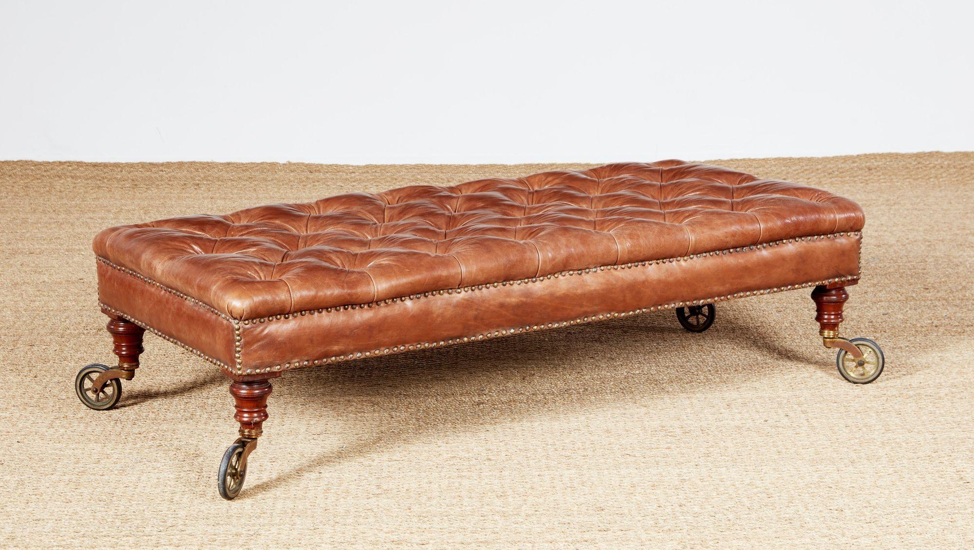Un pouf sostanzioso con un piano imbottito e pannelli laterali delineati da borchie. Rivestito in pelle di selleria color cognac di eccellente qualità. Si erge su gambe tornite che terminano con grandi rotelle girevoli in ottone con bordi in gomma.