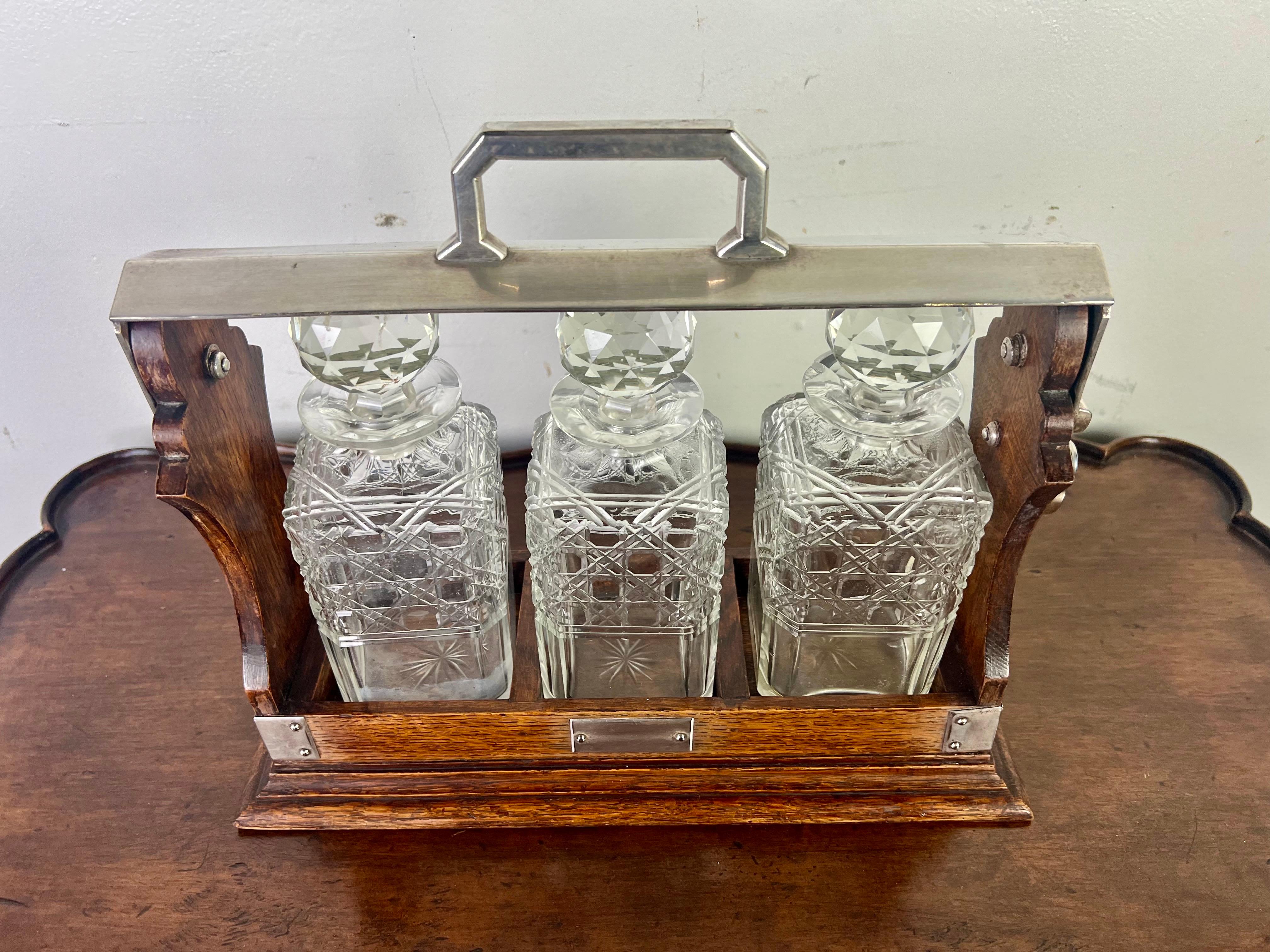 19th C. English decanter set housed in a wooden and metal-framed caddy.  There are three crystal decanters with intricate crosshatched and diamond-patterned designs.  Each decanter has a large, faceted stopper.  The caddy is made of polished oak