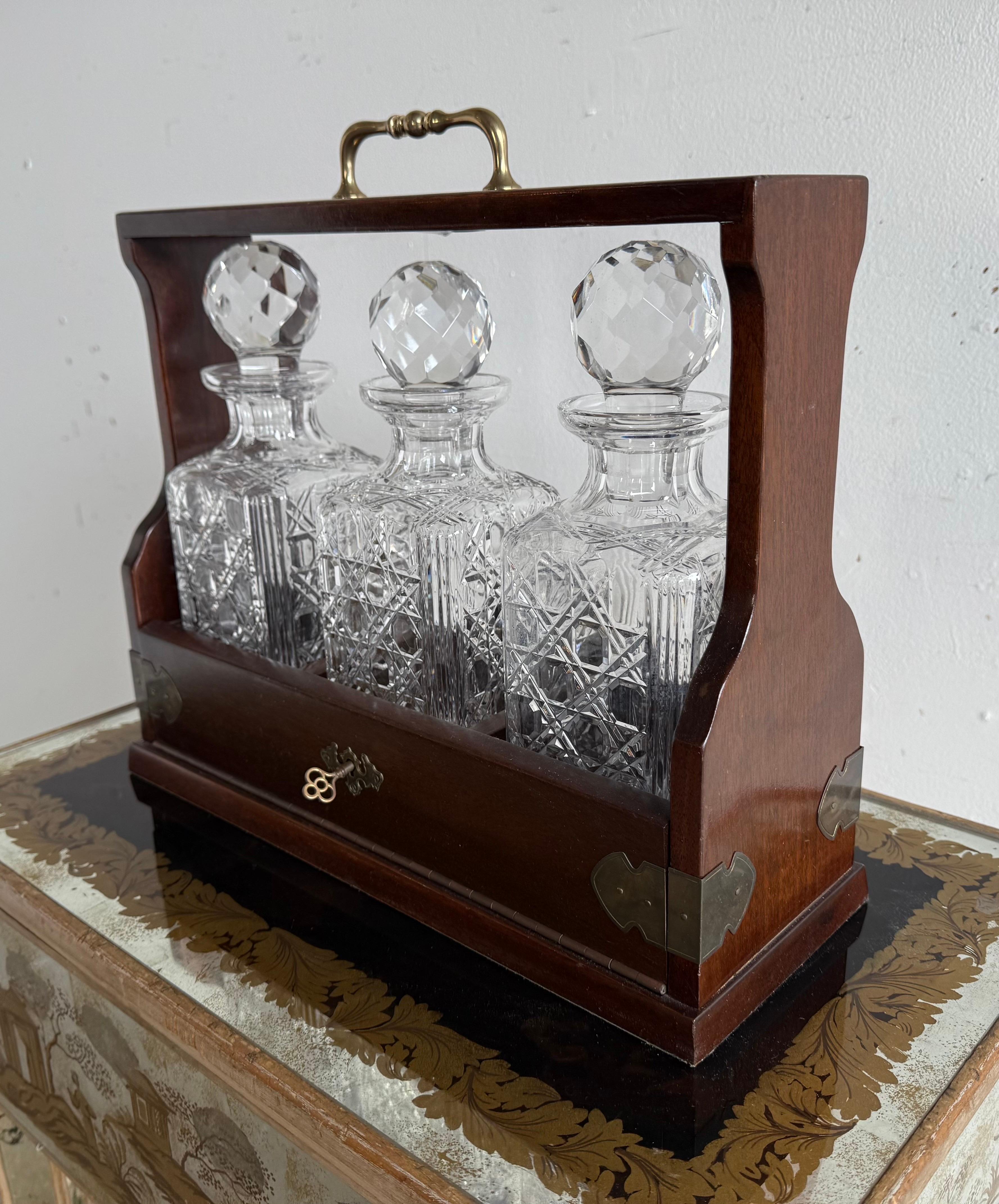 This is a beautifully crafted tantalus, a traditional liquor decanter set designed to secure and display fine spirits.  The set includes three crystal decanters, each with a faceted globe stopper and an intricate cut-glass pattern featuring
