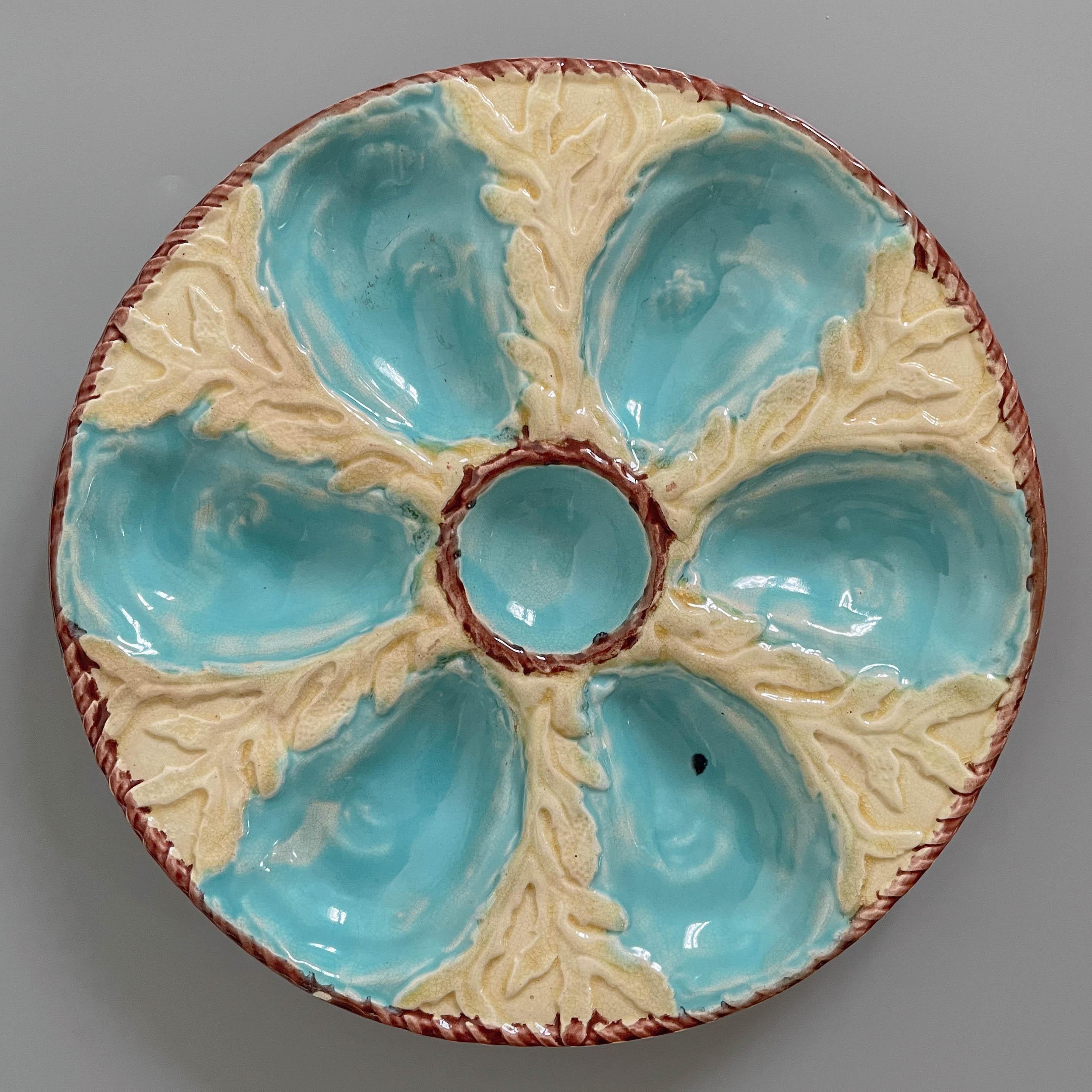 Assiette à huîtres en majolique émaillée anglaise du XIXe siècle, avec six puits à huîtres bleu turquoise entourant un puits central pour la sauce, sur un fond jaune avec relief d'algues. Une bordure de corde nautique brune entoure le puits central