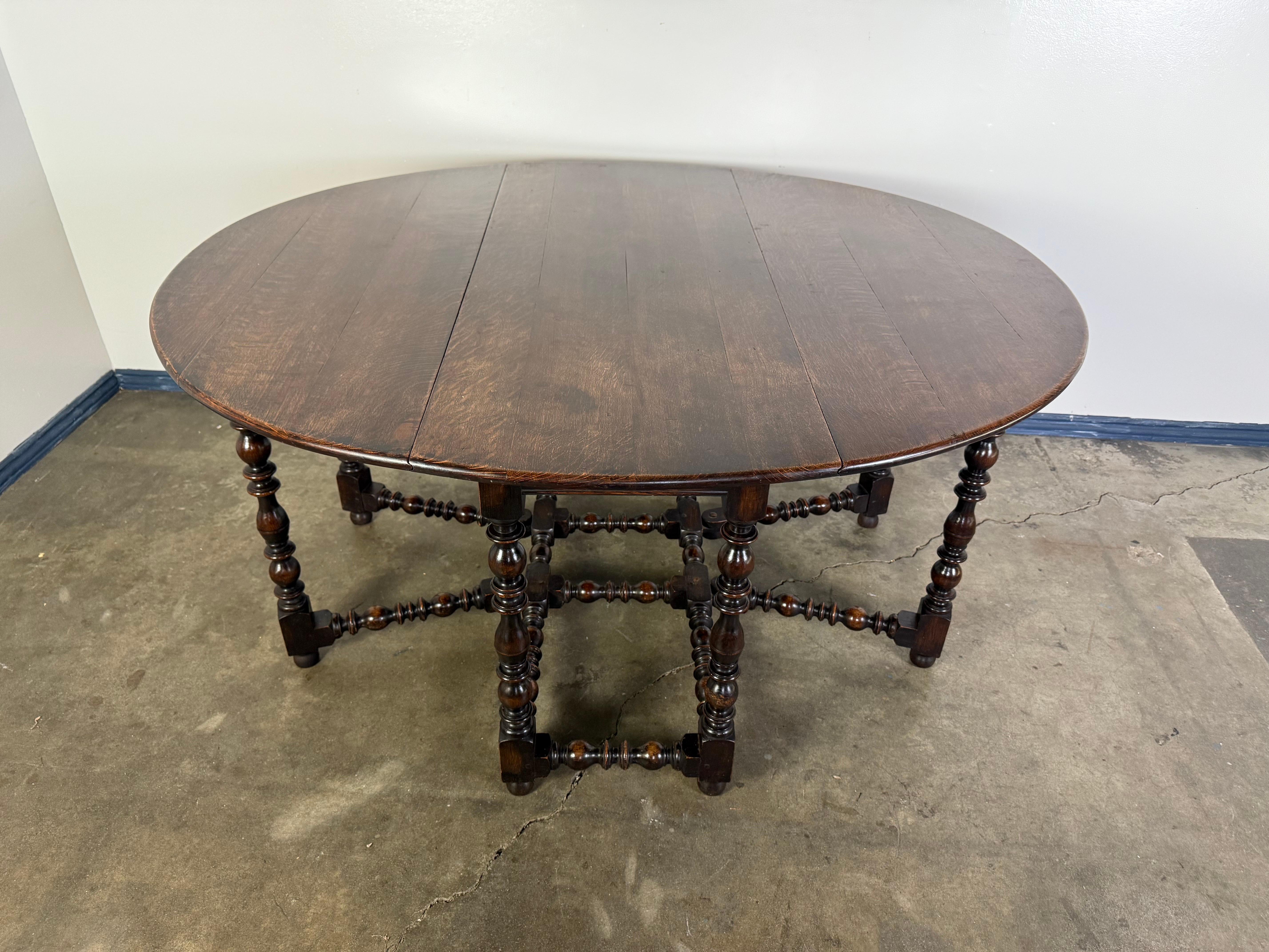 This is a 19th century English gateleg drop-leaf table crafted from dark-stained oak. The oval top features two hinged leaves that can be raised and supported by swinging gateleg supports, making it both functional and space-saving. The table rests