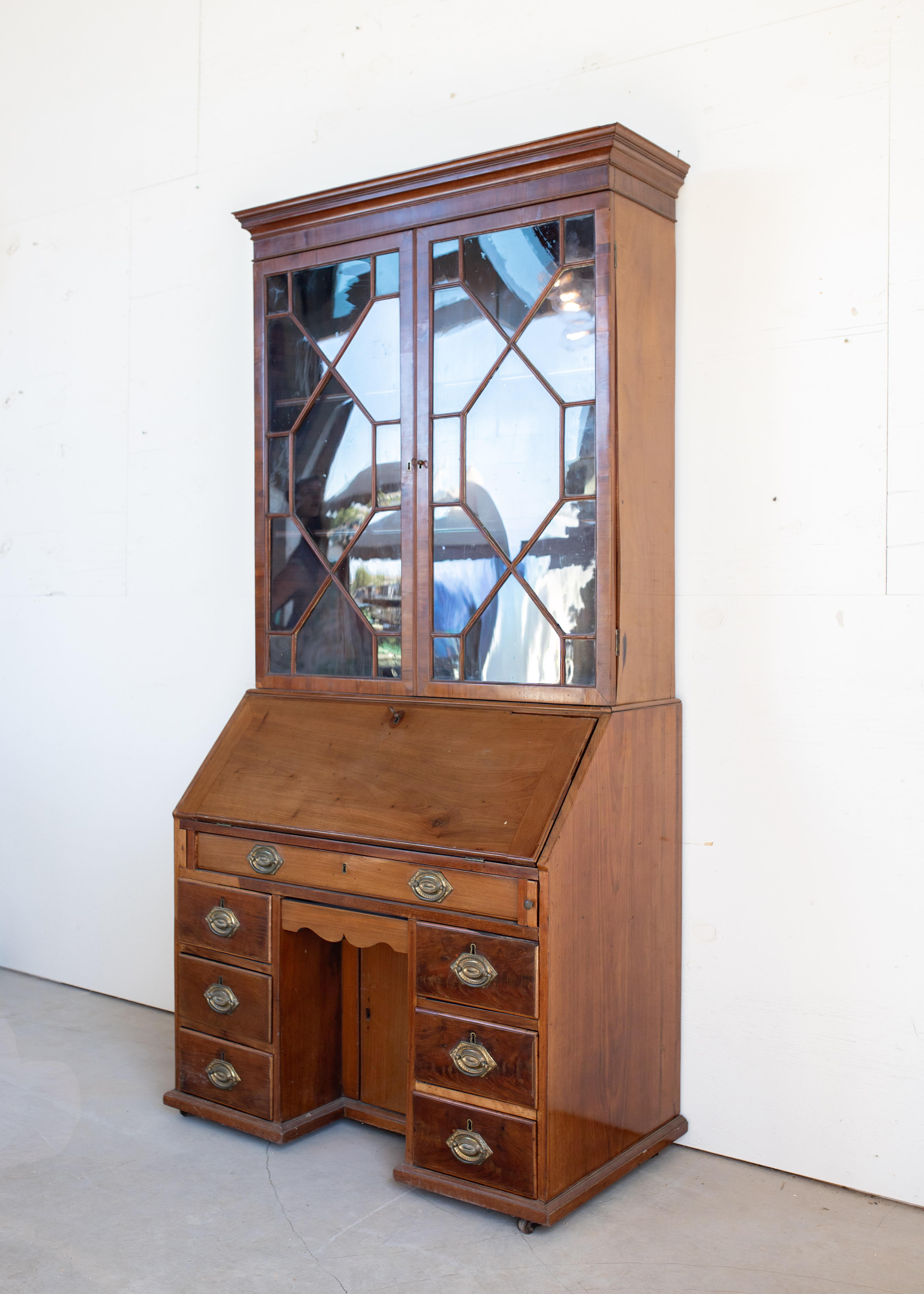 An elegant 19th-century English Georgian mahogany secretaire, combining refined form with practical function. The upper cabinet features original glazed mullioned doors with geometric astragal details, opening to adjustable interior shelving ideal