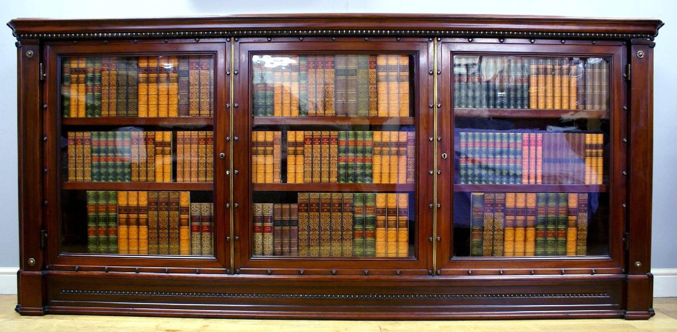 This handsome and well-sized English mahogany bookcase features three glass fronted doors with original locks and key. The bookcase has nicely detailed canted corners and fully adjustable shelves. It measures 94 in – 239 cm wide, 14 ½ in – 37 cm