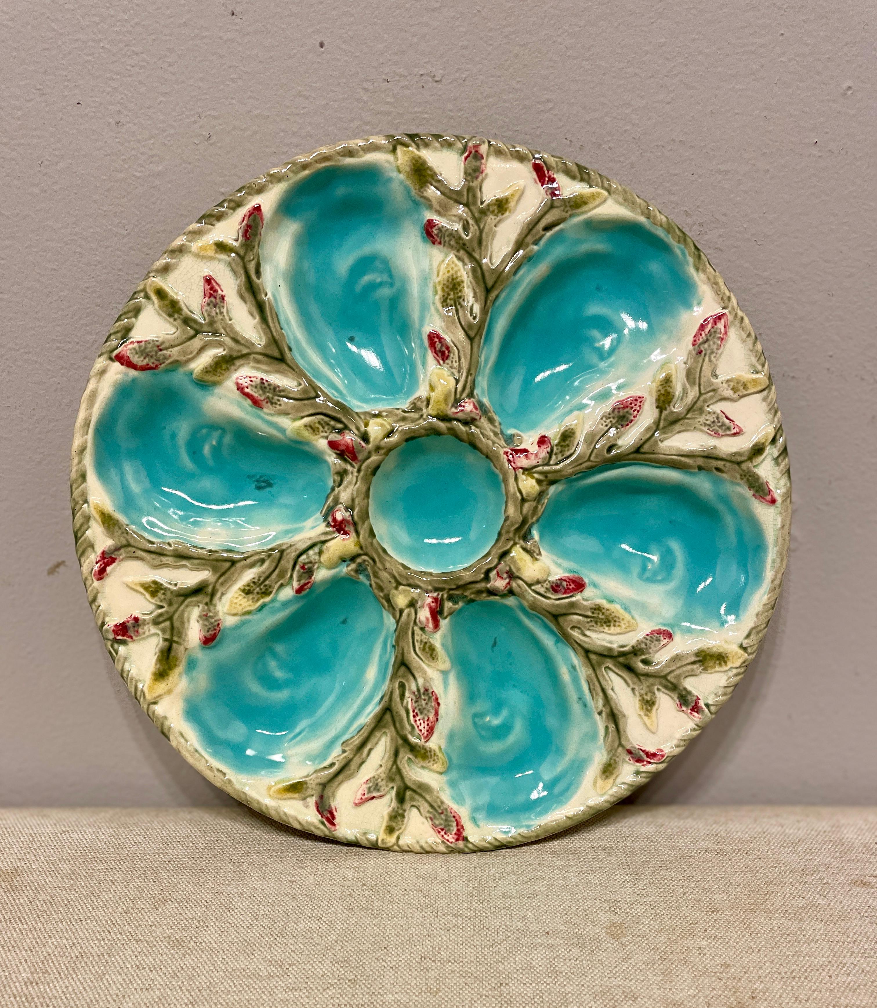 A 19th Century English glazed majolica oyster plate with six turquoise blue oyster wells surrounding a center well for sauce on cream ground with seaweed relief accented with yellow and red. A pale green nautical rope border encircles the center