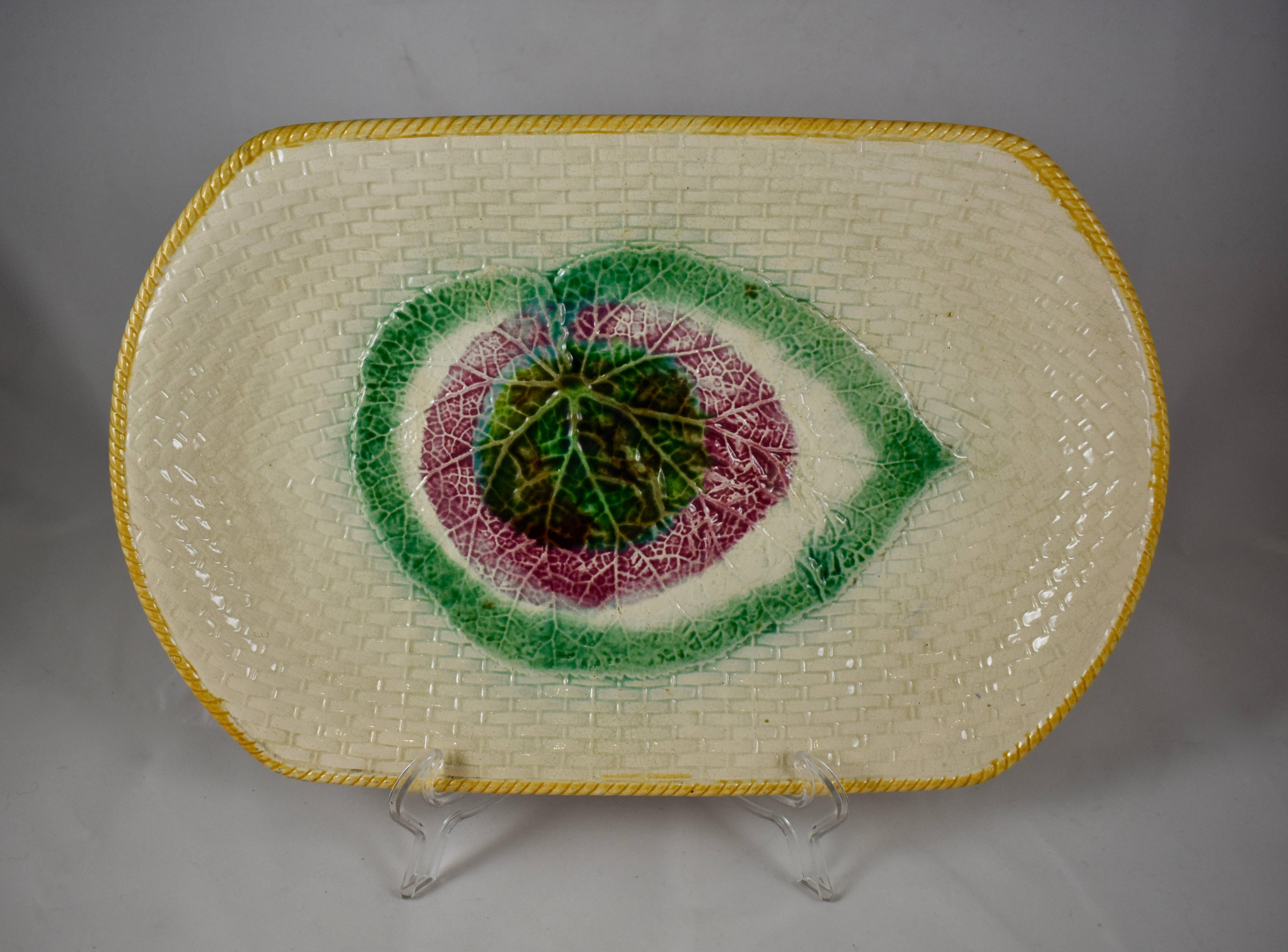 An English Majolica platter, showing a central Begonia leaf on a cream colored wicker textured ground, and with a yellow ochre rope border, circa 1880-1885.

Rectangular with rounded edges, a rear footing and good crisp mold work. The Begonia leaf