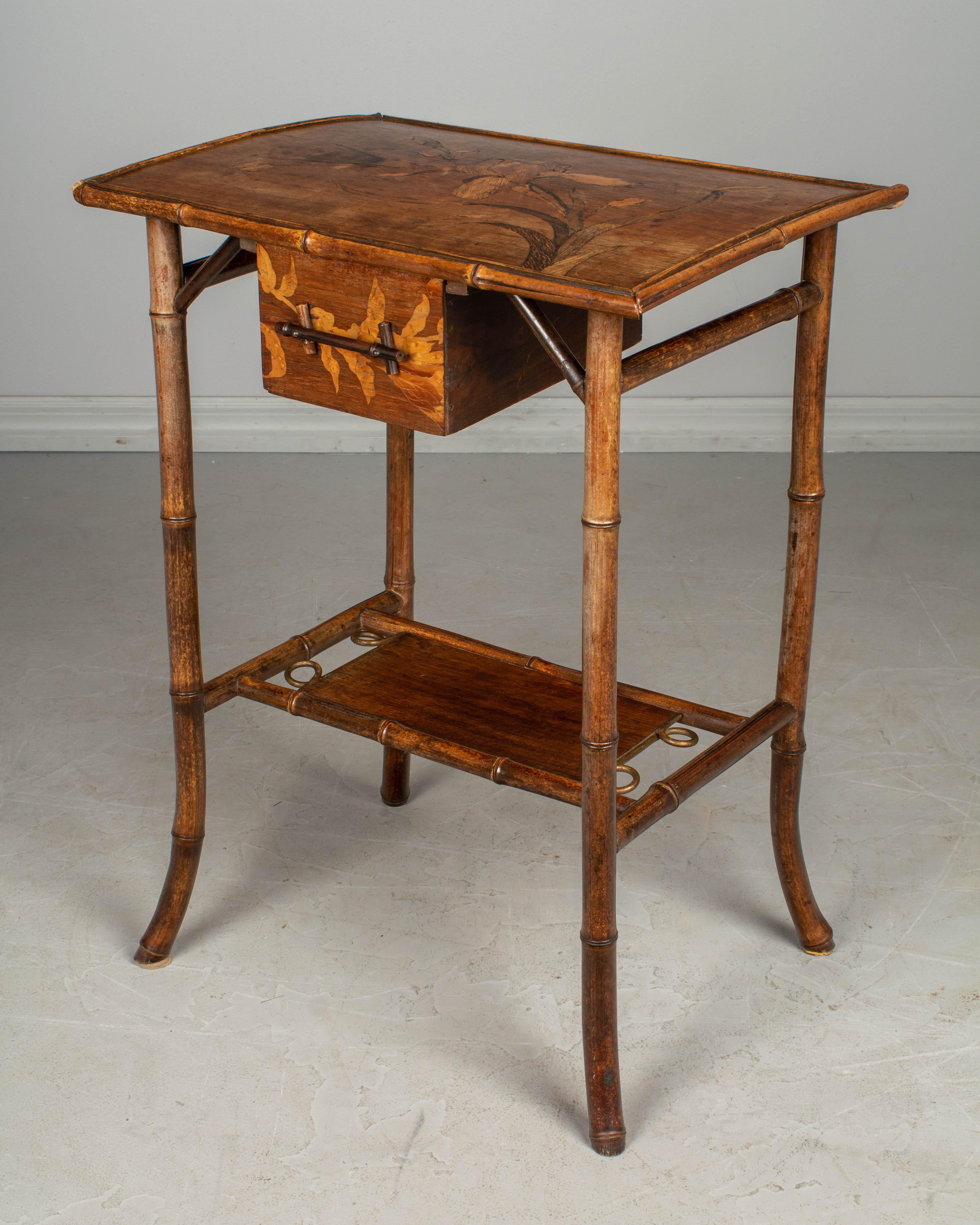 A 19th century English Art Nouveau bamboo side table with marquetry top, a lower shelf and small drawer. The top has an inlaid marquetry iris flower and is slightly warped. Please refer to photos for more details.
 