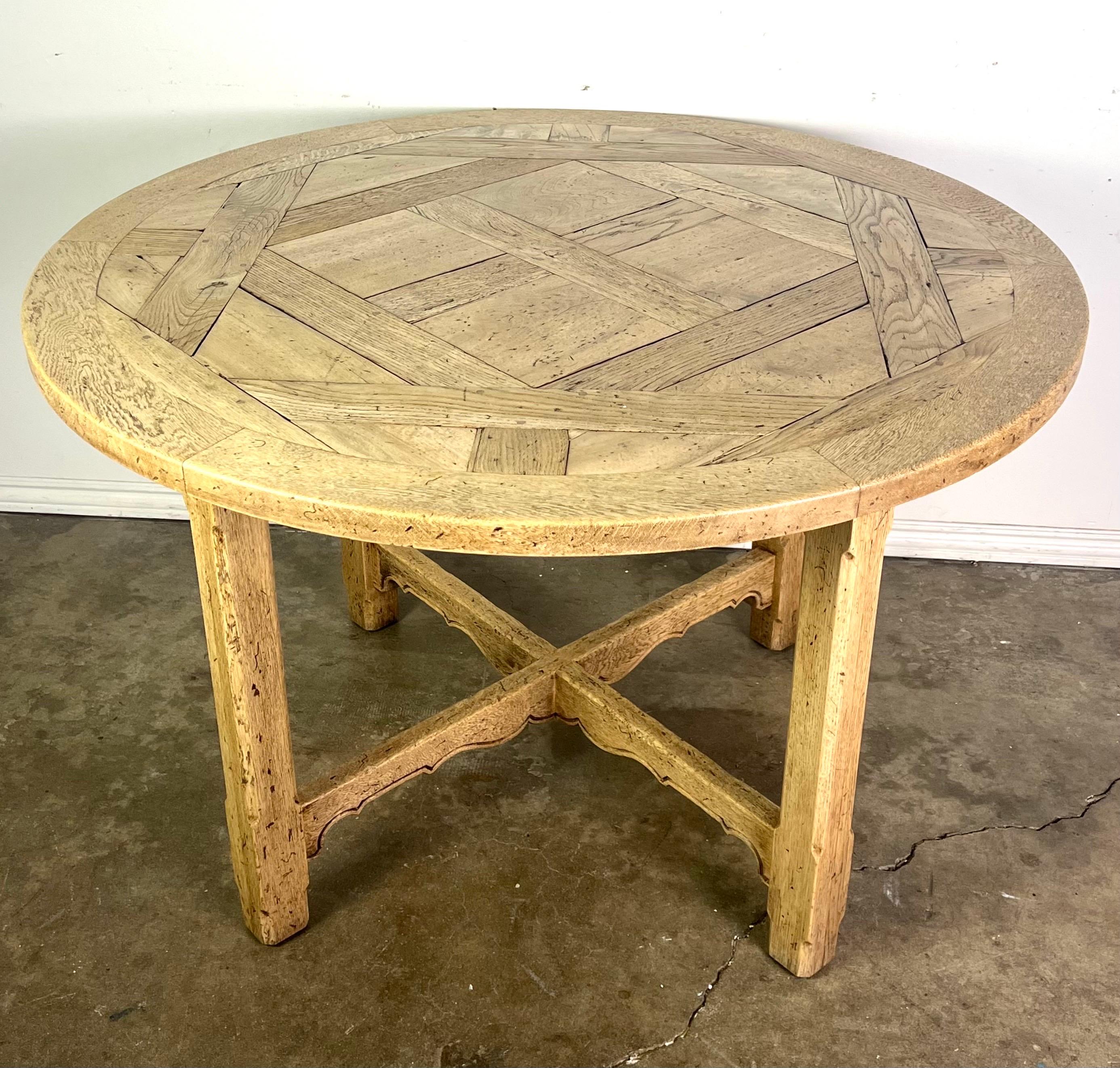 19th C. English round wooden table with a rustic, handcrafted appearance.  The tabletop has an intricate design, with sections of wood arranged in a geometric, parquet-like pattern, adding texture and visual interest.  The wood is light in color,