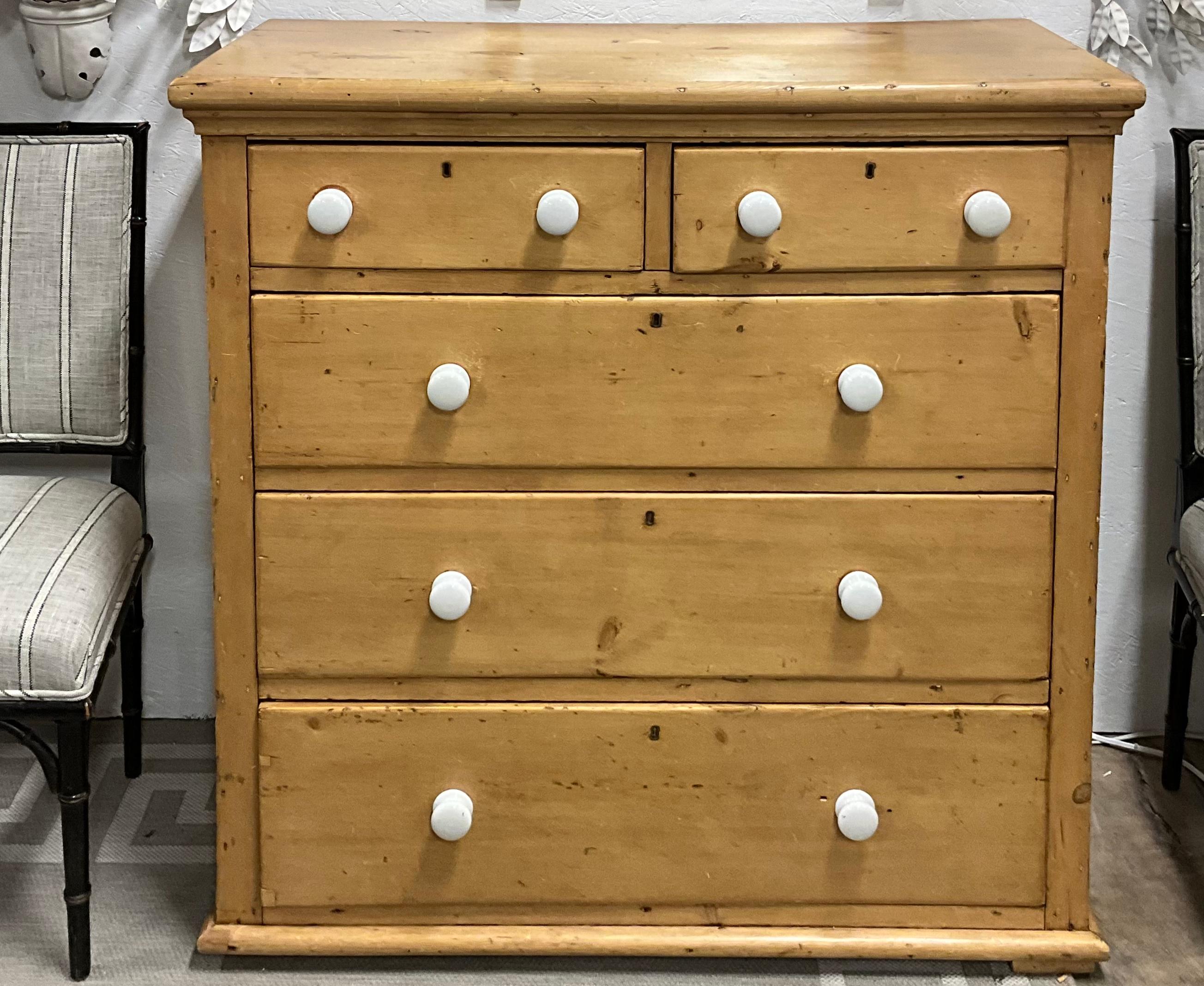 This is a wonderful antique pine chest! It is English and dates to the later part of the 19th century. The knobs are porcelain and appear to be original. Furthermore, someone has meticulously lined each drawer with blue and white ticking paper. I