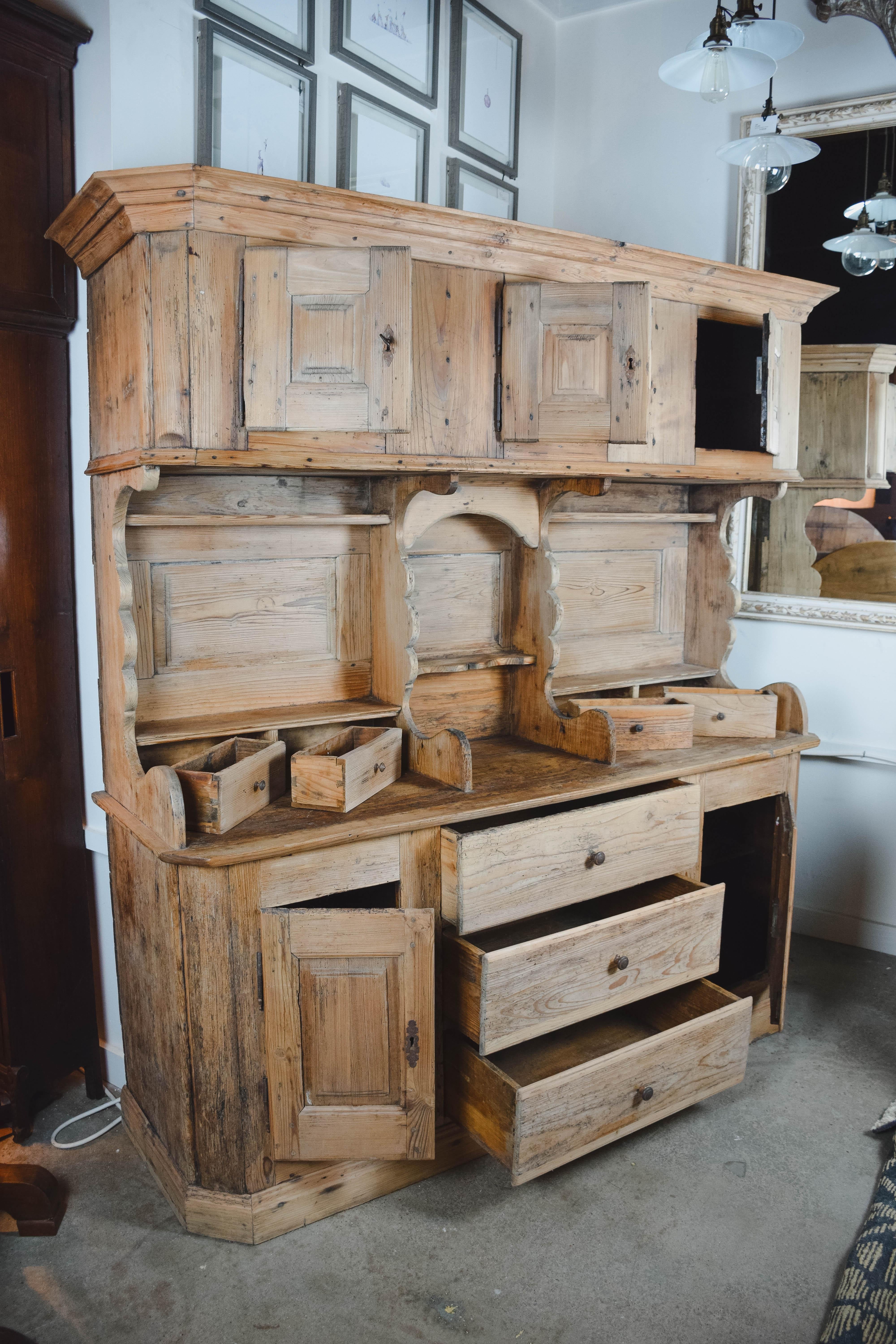 From England, this Classic country antique pine hutch has a beautiful aged patina. The cupboard has tons of storage space with three upper doors, each with a shelf inside along with a small exposed shelf below, four small drawers above the serving