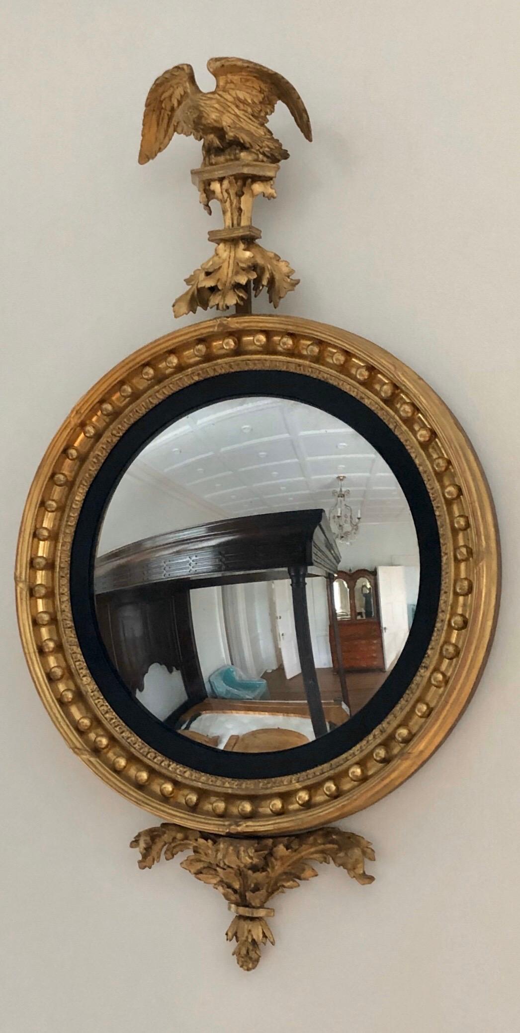 This Regal period Regency giltwood bulls eye mirror has an giltwood carved eagle perched on a giltwood foliate plinth. The eagle is cresting over a convex mirror with gilt frame surrounded by ball decoration with an ebonized slip. The convex is