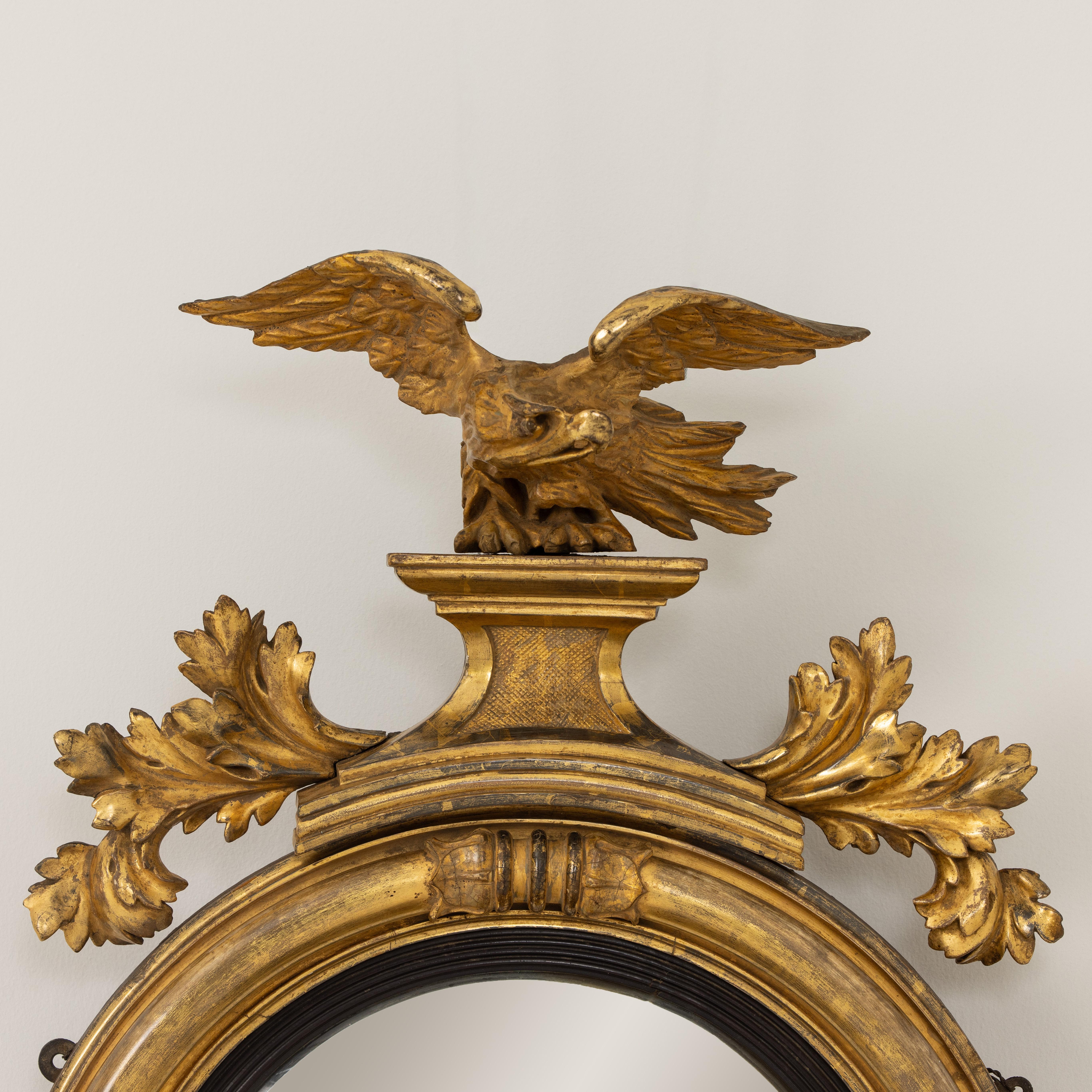 A fine Regency original giltwood mirror with convex mirror plate. The frame features carved lotus flower terminals meeting at the four compass points. The mirror is topped by a cresting of an eagle on a pedestal with leafy branches below. At the
