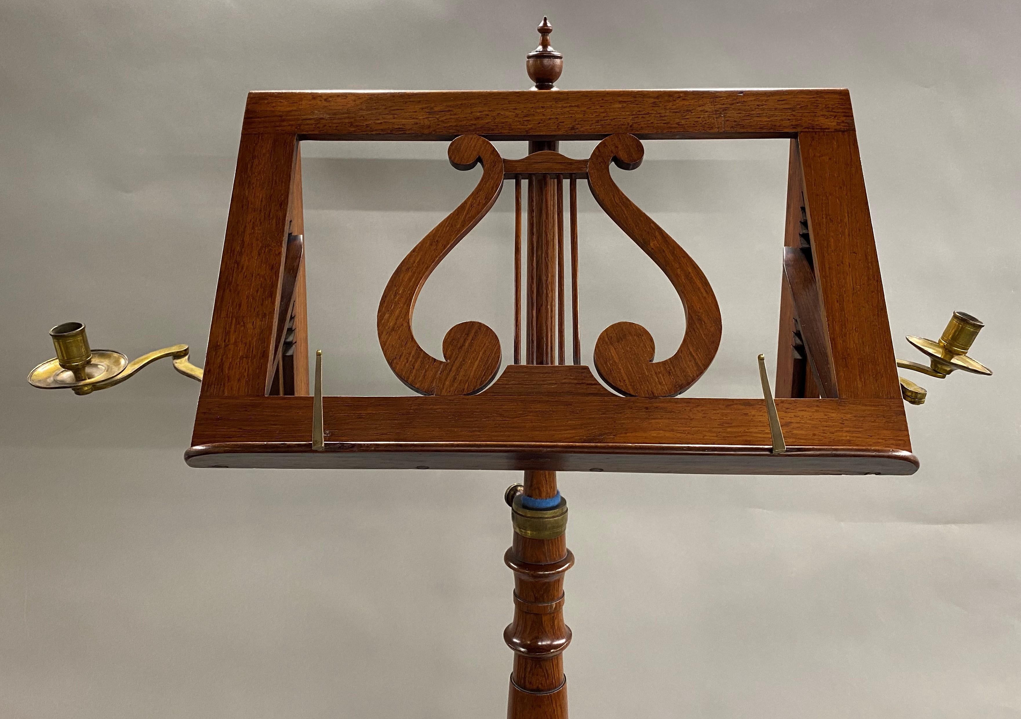 A fine example of an English rosewood music stand with adjustable lyre form tray, with hinged extending brass candle sconces on each side, turned pedestal with adjustable height, on a tripod base with bun feet. Dates to the early 19th century in