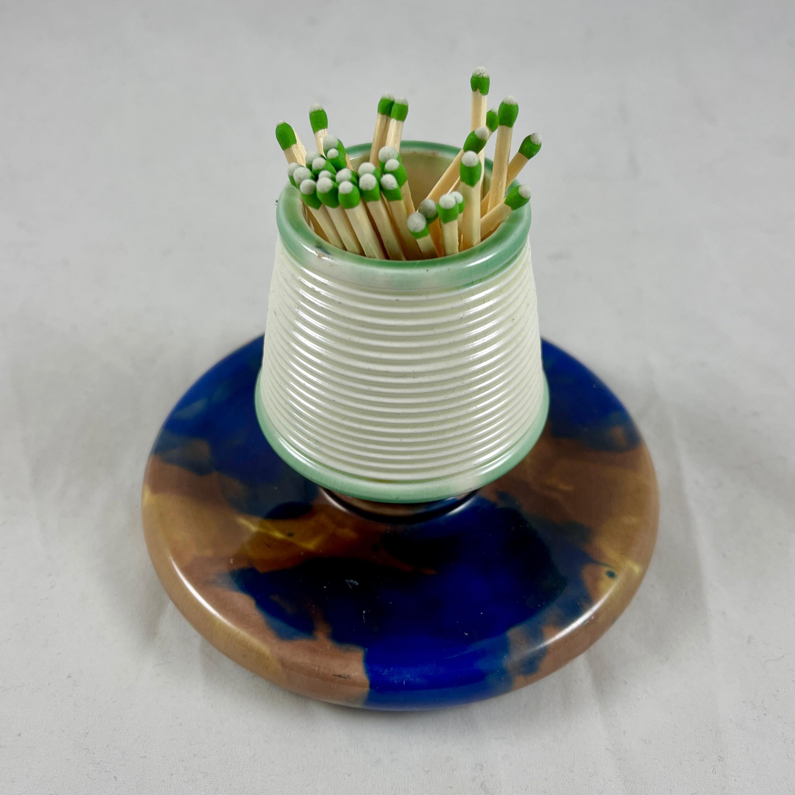 A wedgwood Majolica earthenware pottery match holder and striker, Staffordshire, England – dated 1882.

For the hearth, kitchen or bedside, the holder is ribbed for lighting strike-anywhere matches, the bottom tray is for the spent sticks. The