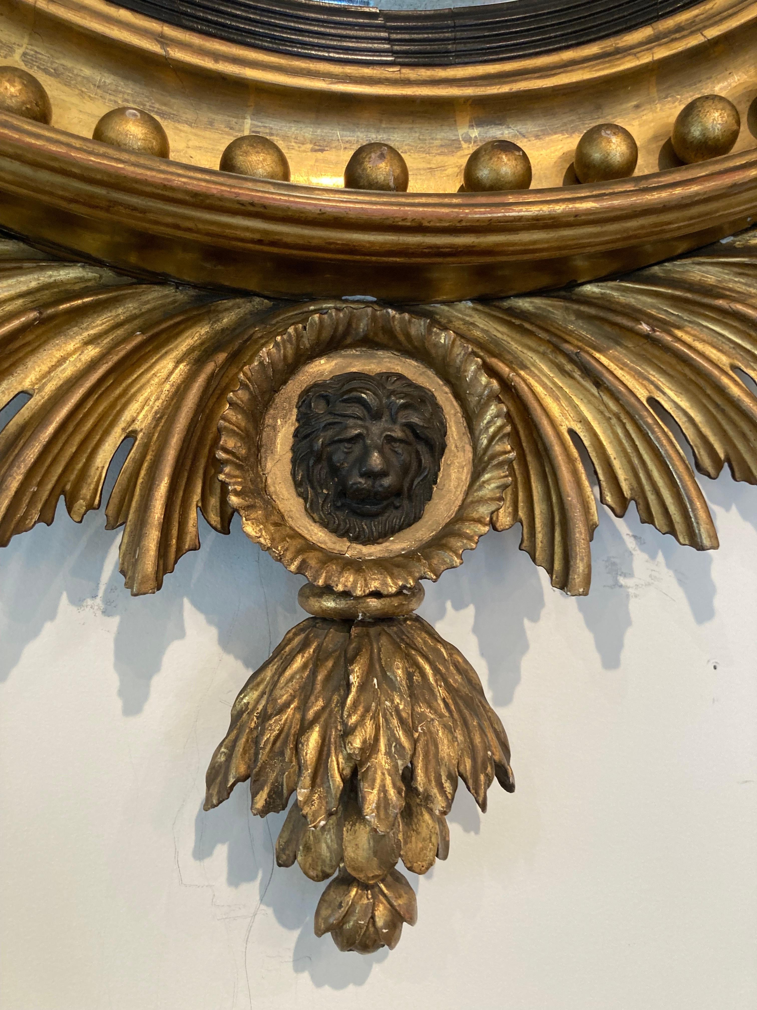 Elégant miroir convexe du 19ème siècle dans un cadre en bois doré avec une coiffe d'aigle noire. 4 bras de bougie en métal doré et un médaillon à face de lion noir. Style fédéral.