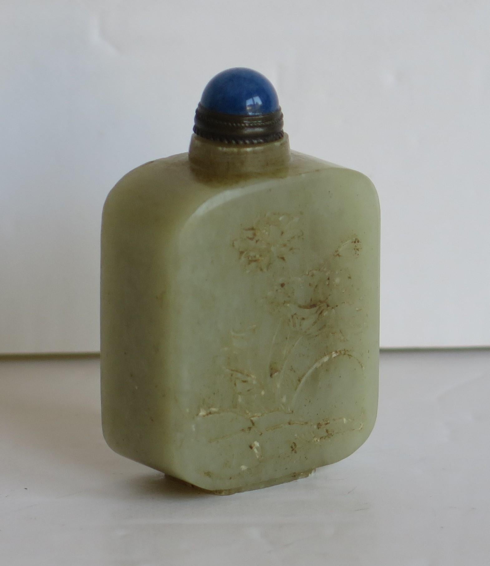 This is a beautiful Chinese snuff bottle, well carved and made from a stone with a light celadon green colour that we attribute as being nephrite .

The bottle has a lovely light green celadon color and sits on a low foot. It has two different hand