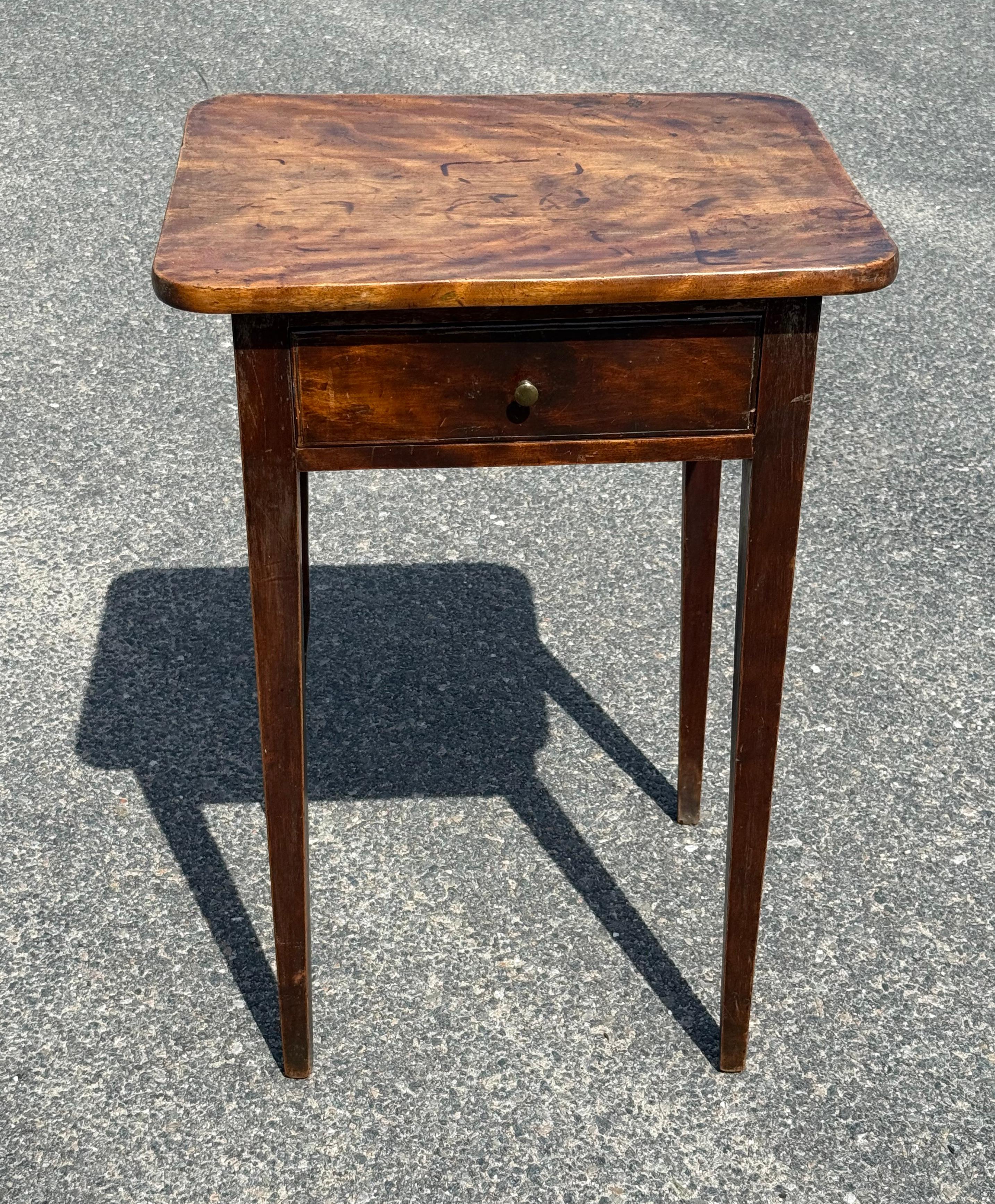 Sweet little 19th century single drawer side table in original finish.  Pretty flame birch top with rounded corners over single drawer with (replaced) brass pull), taper legs.  Rear left leg with slight bend due to section of wood used and carved