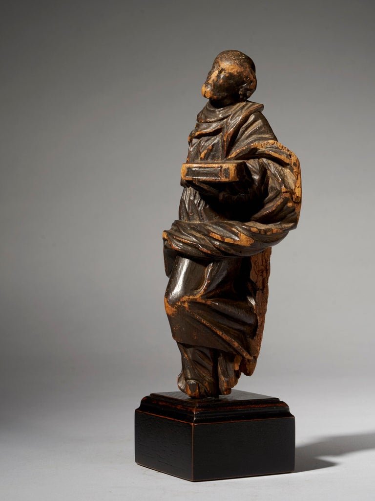 This sculpture represents Moses holding the ten Commandments. It is carved from a single piece of wood and has an upper layer of varnish. The wood shows signs of aging and has a nice patina.