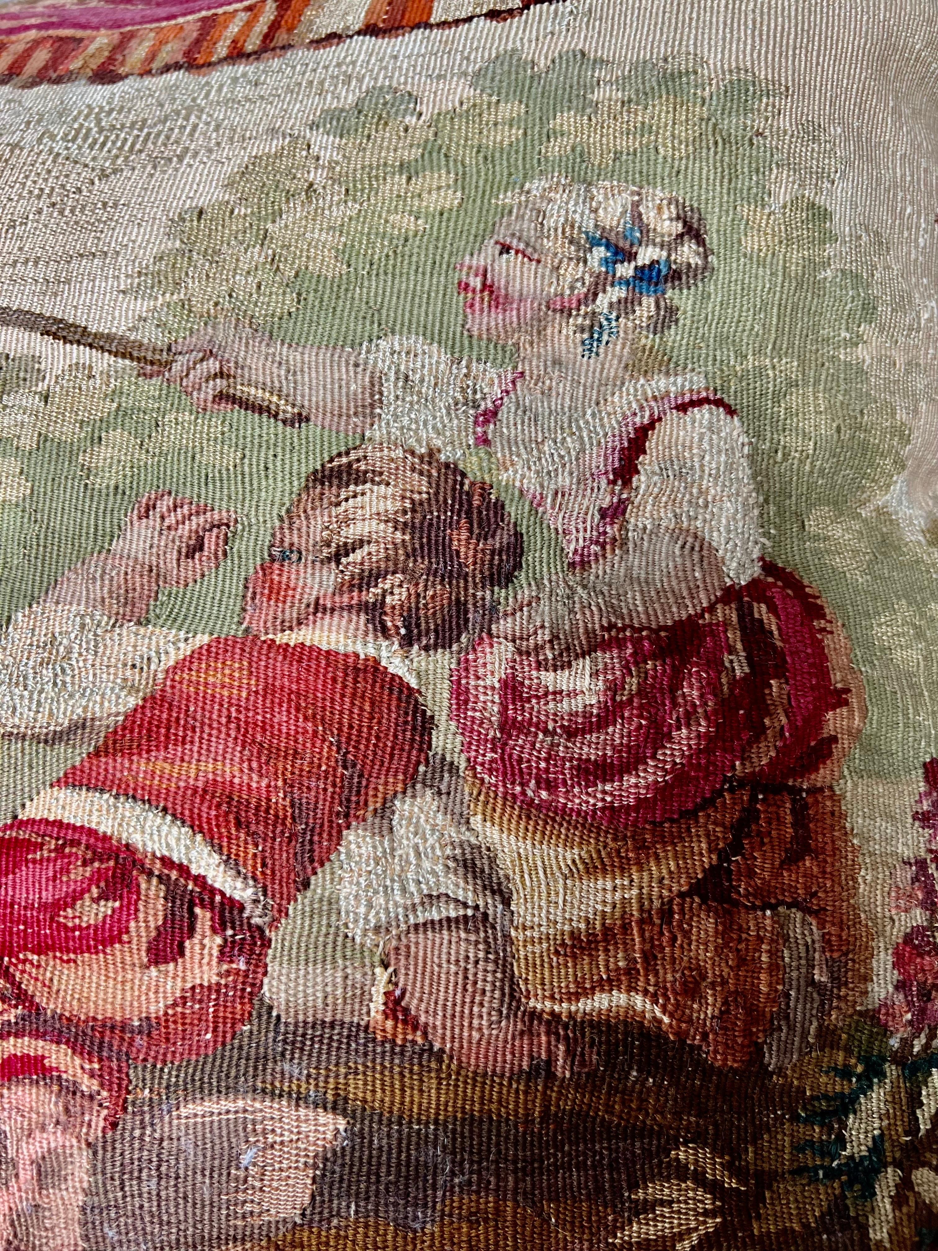 The 19th-century Aubusson bed pillow is a charming piece, depicting a scene of children playing a blindfolded game with a little dog in the background.   The garlands of fabric and tassels create a theatrical touch.  Multicolored fringe on the sides