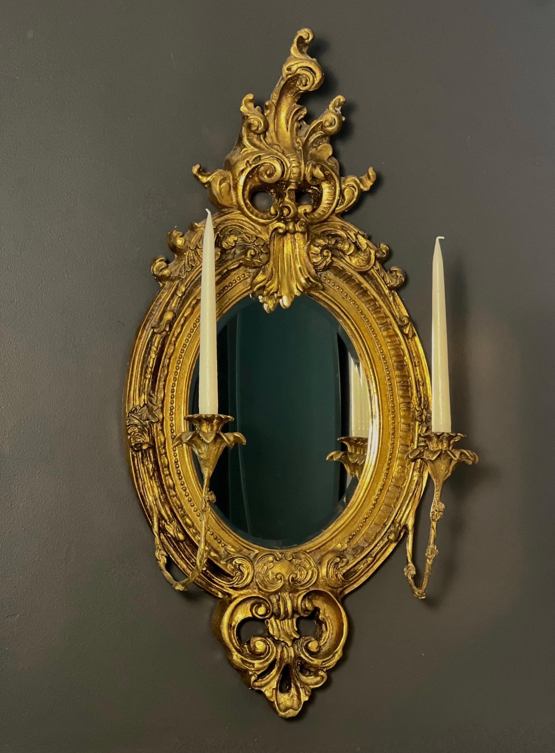 Stunning antique carved gilt girandole mirror in the Baroque manner with two candelabra, France, ca. 1890. An oval form, beveled mirror framed by a robust and lavishly carved and molded giltwood frame of scrolls, acanthus leaves and highly detailed