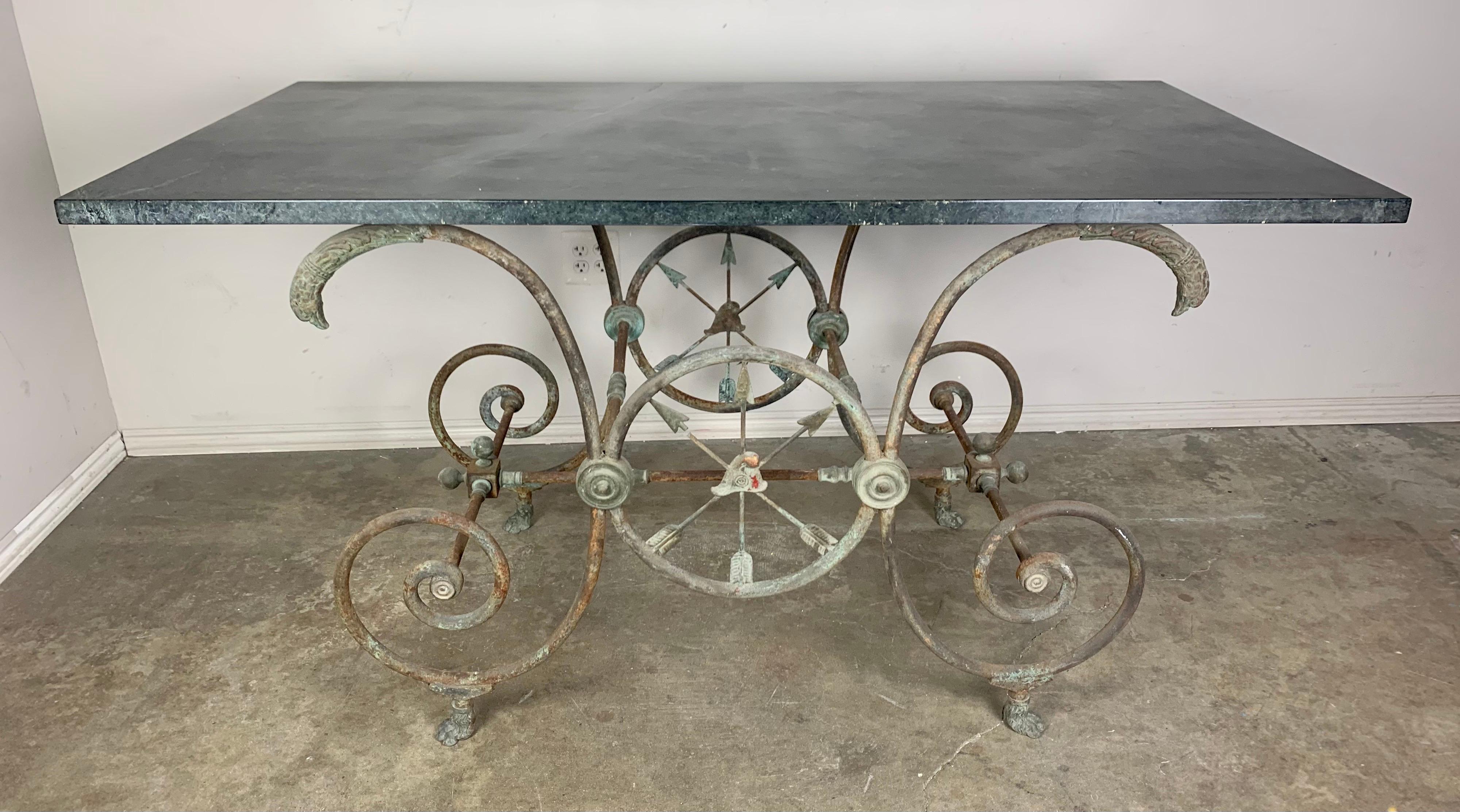 19th century French bistro table with marble top. The wrought iron and bronze base depict circle with crossed arrows. There are bird heads at the top of the scrolled bases that hold up the marble top. The are beautiful details throughout this bistro