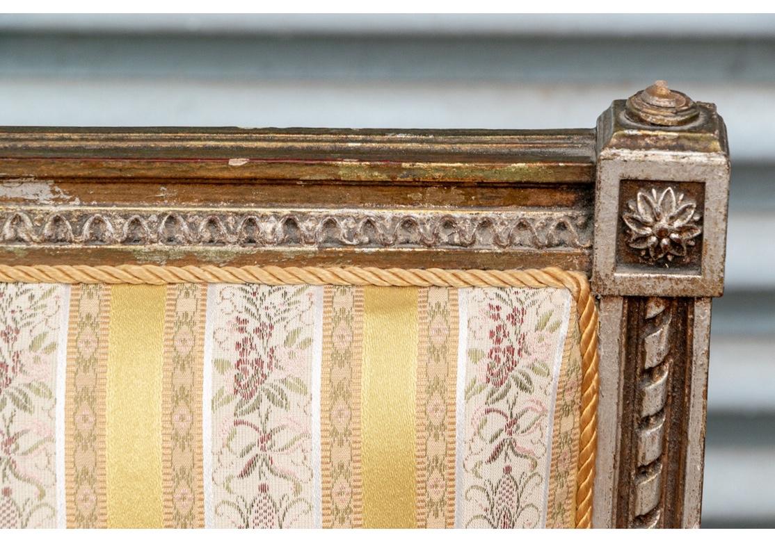 The elaborate crest rail with carved crest of berries and leaves and musical motifs in the center- a mandolin, a horn and curled sheet music. The carved ends with rosettes and small finials. The sloping supports with ribbon twist bands, the arms
