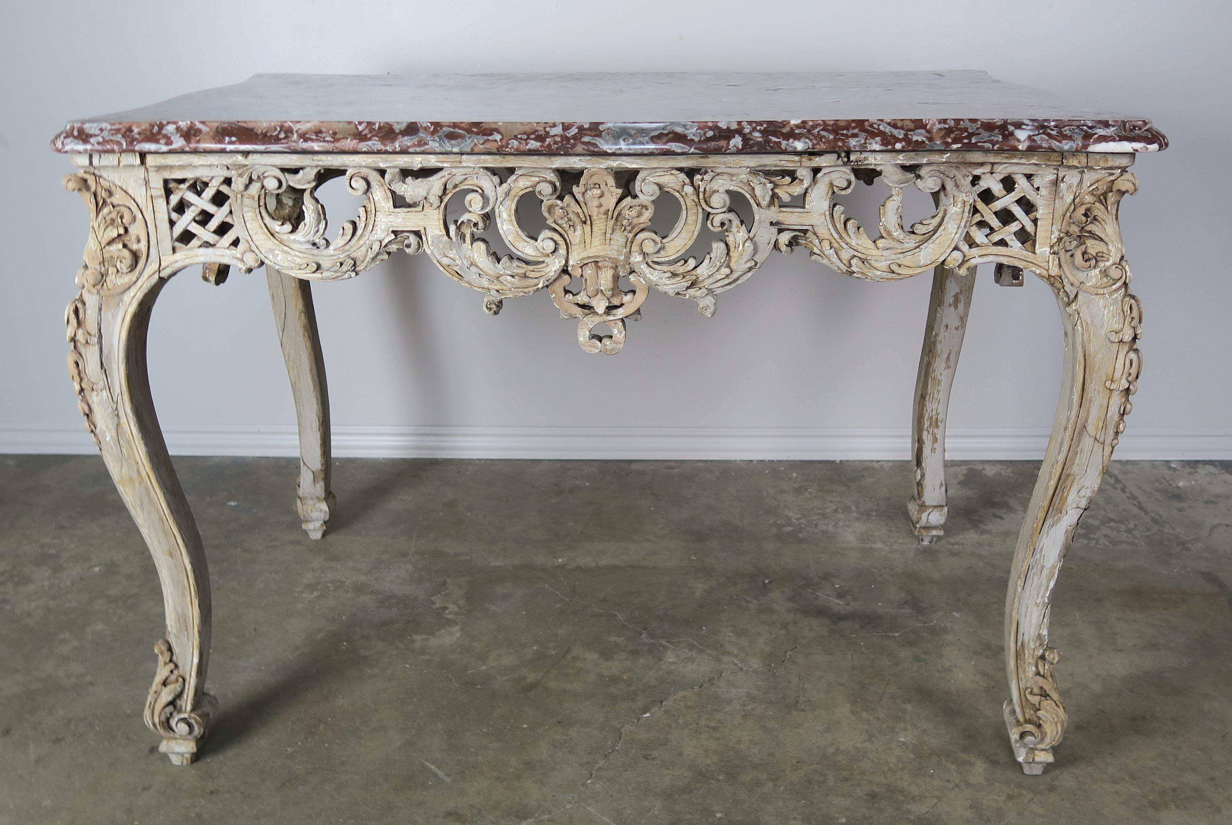 19th century French finely carved table standing on four cabriole legs with remnants of antique paint throughout. The table base holds the original rust colored marble top with a beautiful single ogee bullnose edge detail. Intricate carved details