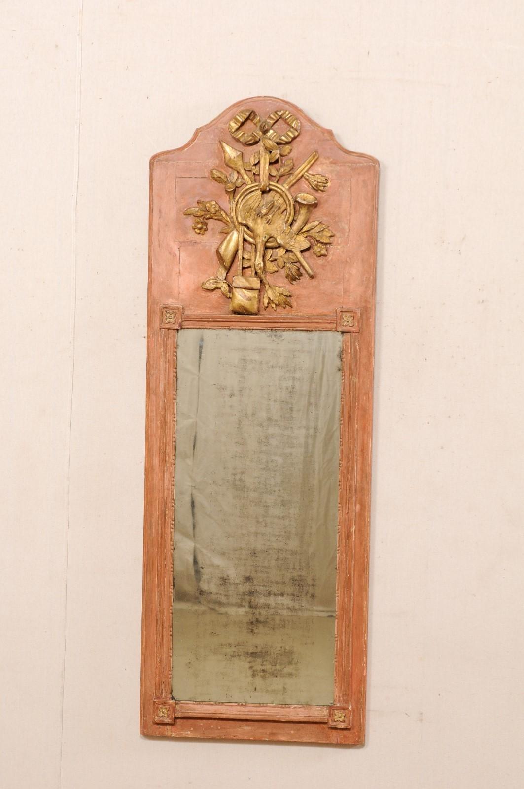 A French carved wood trumeau mirror, with country manor themed carvings, from the 19th century. This antique mirror from France is rectangular-shaped, set in vertical fashion, and features an arched crest top, with raised carvings adorning the upper