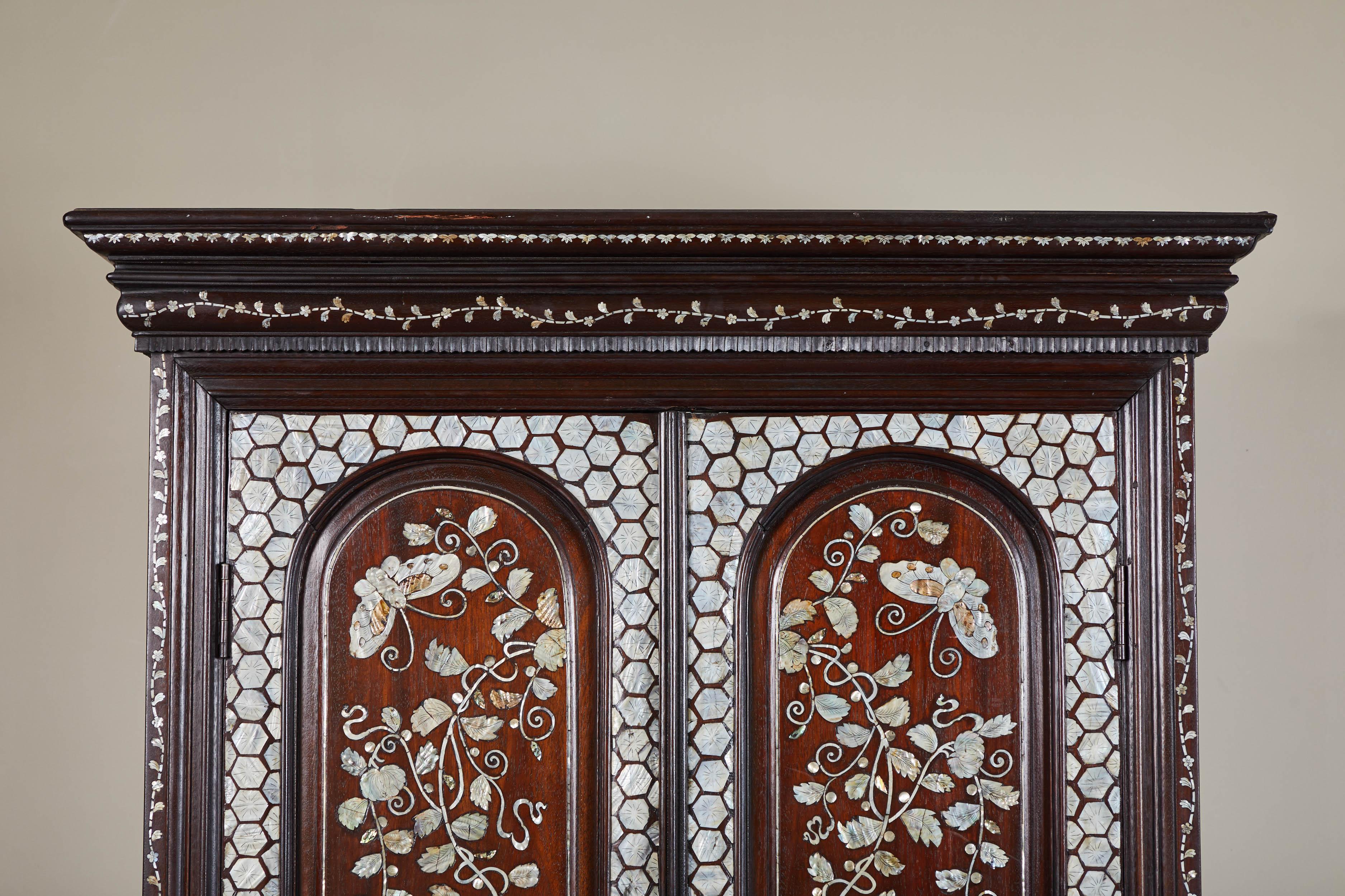 19th century French colonial cabinet with mother-of-pearl inlay along all panels. Hexagonal mosaic along door trim, with floral and butterfly motif throughout door fronts, along feet and top molding.