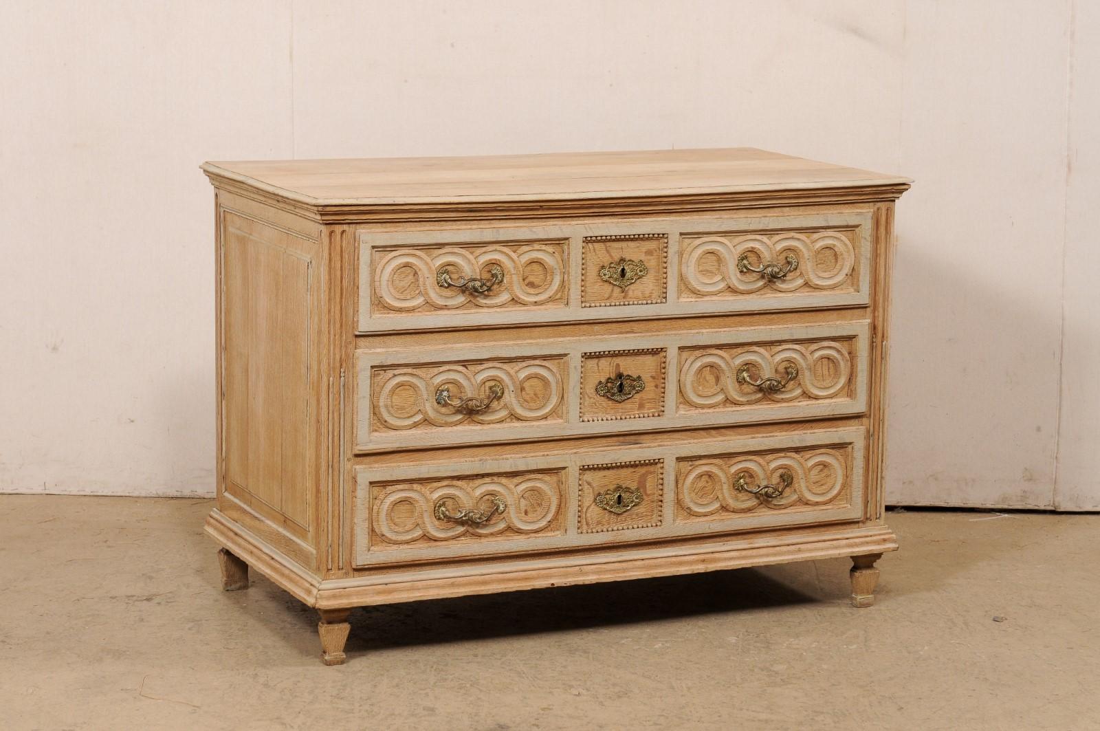 A French carved and bleached wood chest of drawers from the 19th century. This antique commode from France has a rectangular-shaped top over a case which houses three full-sized drawers framed within fluted front side-posts, and presented upon