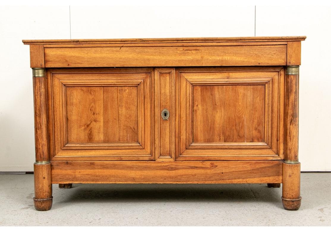 With a panel constructed top that lifts up with hinges at the back. With double carved recessed panel doors opening to a shelf. With a wreath form brass escutcheon and a key. The cabinet with half column supports with decorated brass details. Panel