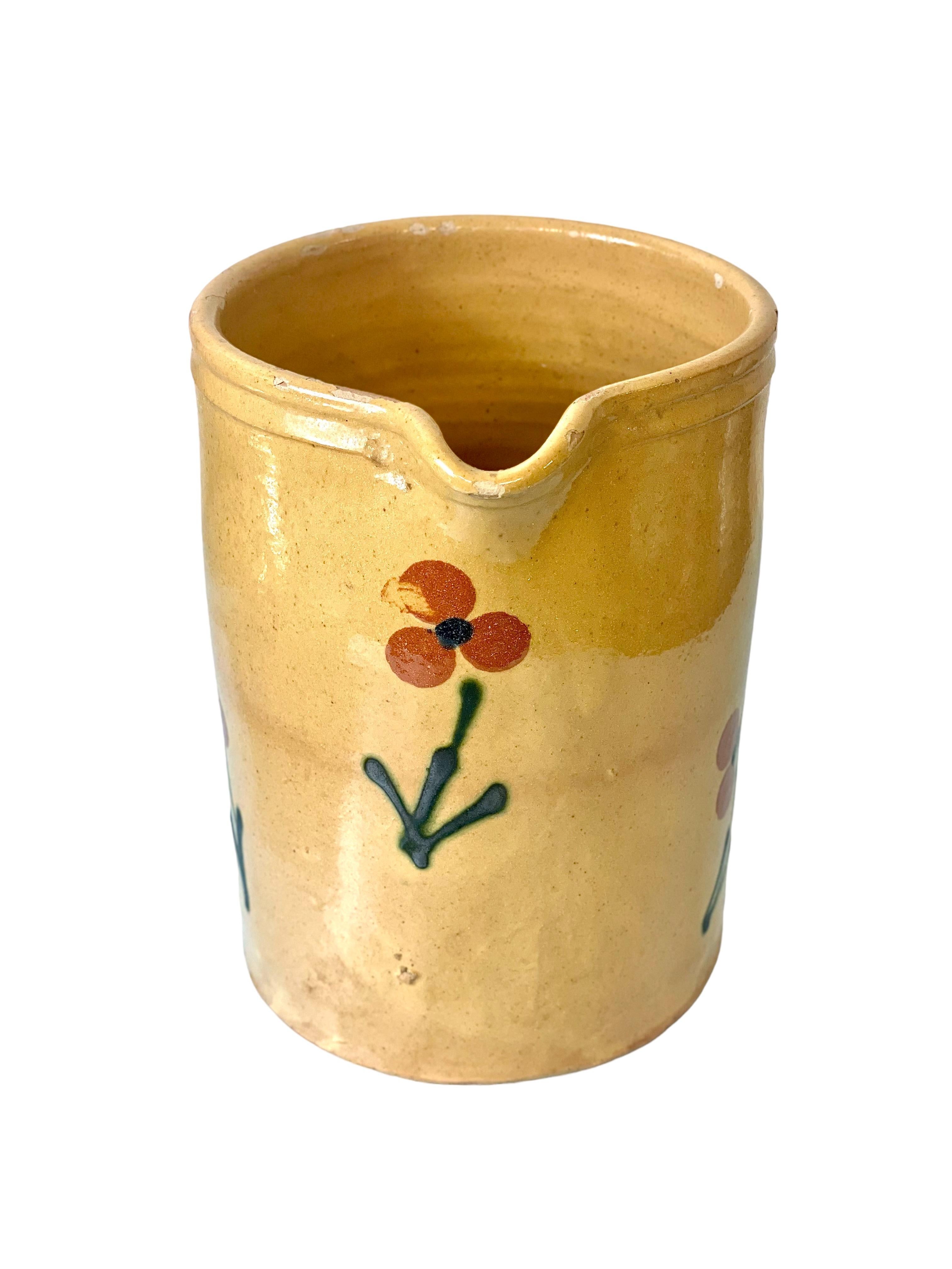 A very pretty 19th century glazed terracotta water pitcher, from the Provence region of southern France. Glazed inside and out in a delicious creamy beige, the exterior has been hand-painted with a simple but classic design of red flowers. A handle