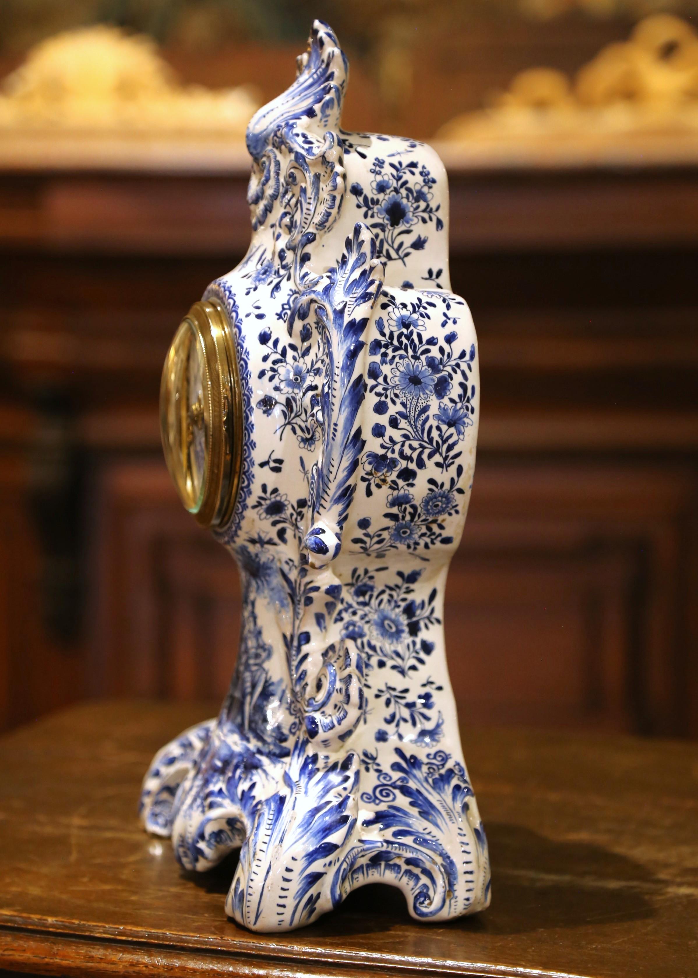 Este ornamentado reloj de chimenea francés se fabricó hacia 1860 en estilo Delft, con loza azul y blanca pintada a mano y ricas florituras rococó. La caja del reloj está decorada con hojas de acanto, aerosoles florales y una romántica escena