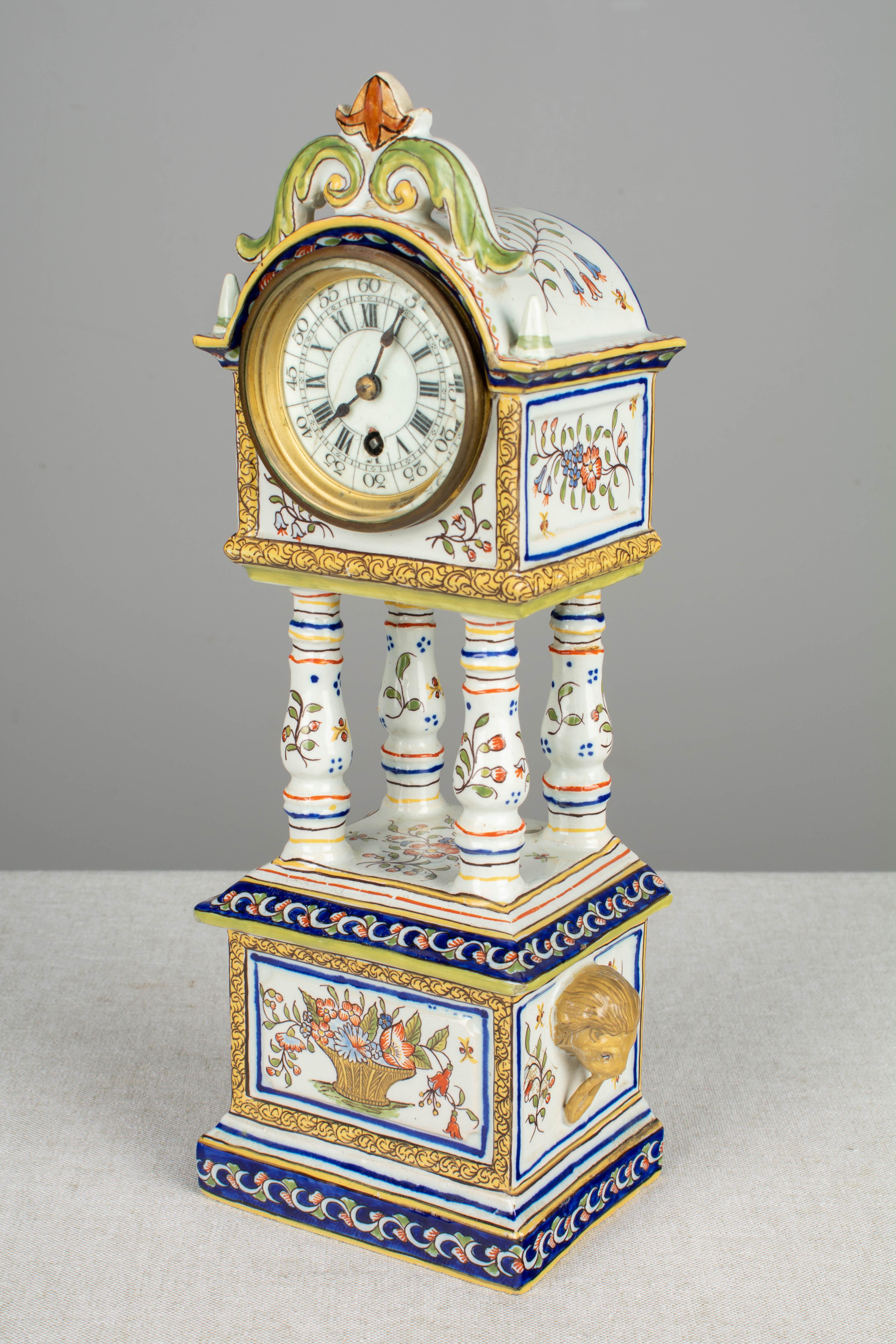 A 19th century French Desvres faience mantle clock, with hand painted floral decoration in the traditional colors of blue yellow, green and orange. Plinth base with lion head prunts on each side and raised on four columns. Arched crown with a small