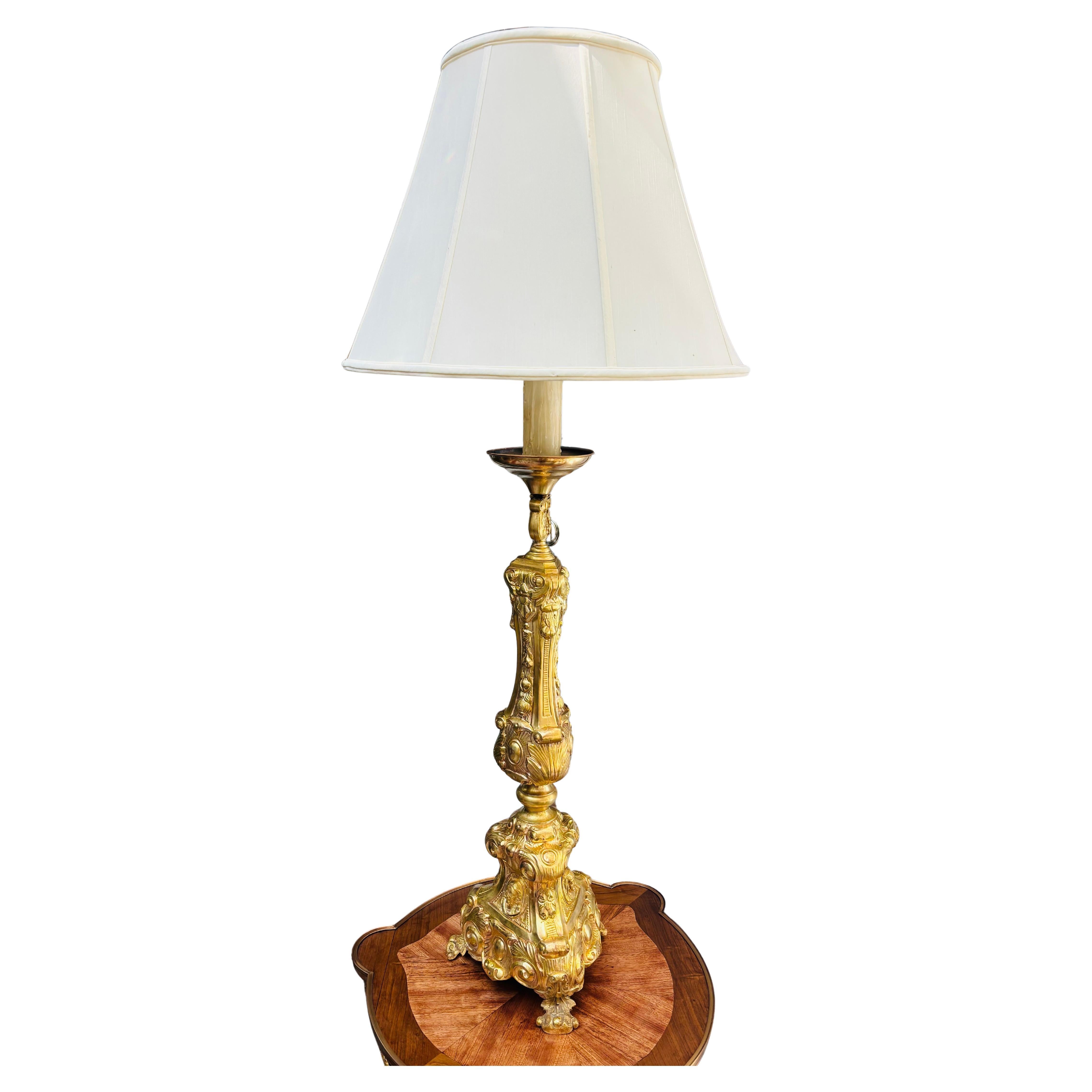 A  triangular embossed  brass metal ecclesiastical candlestick converted into a lamp. The candlestick is made up of  four sections of embossed  brass sheet metal plus a top cup which holds a 10