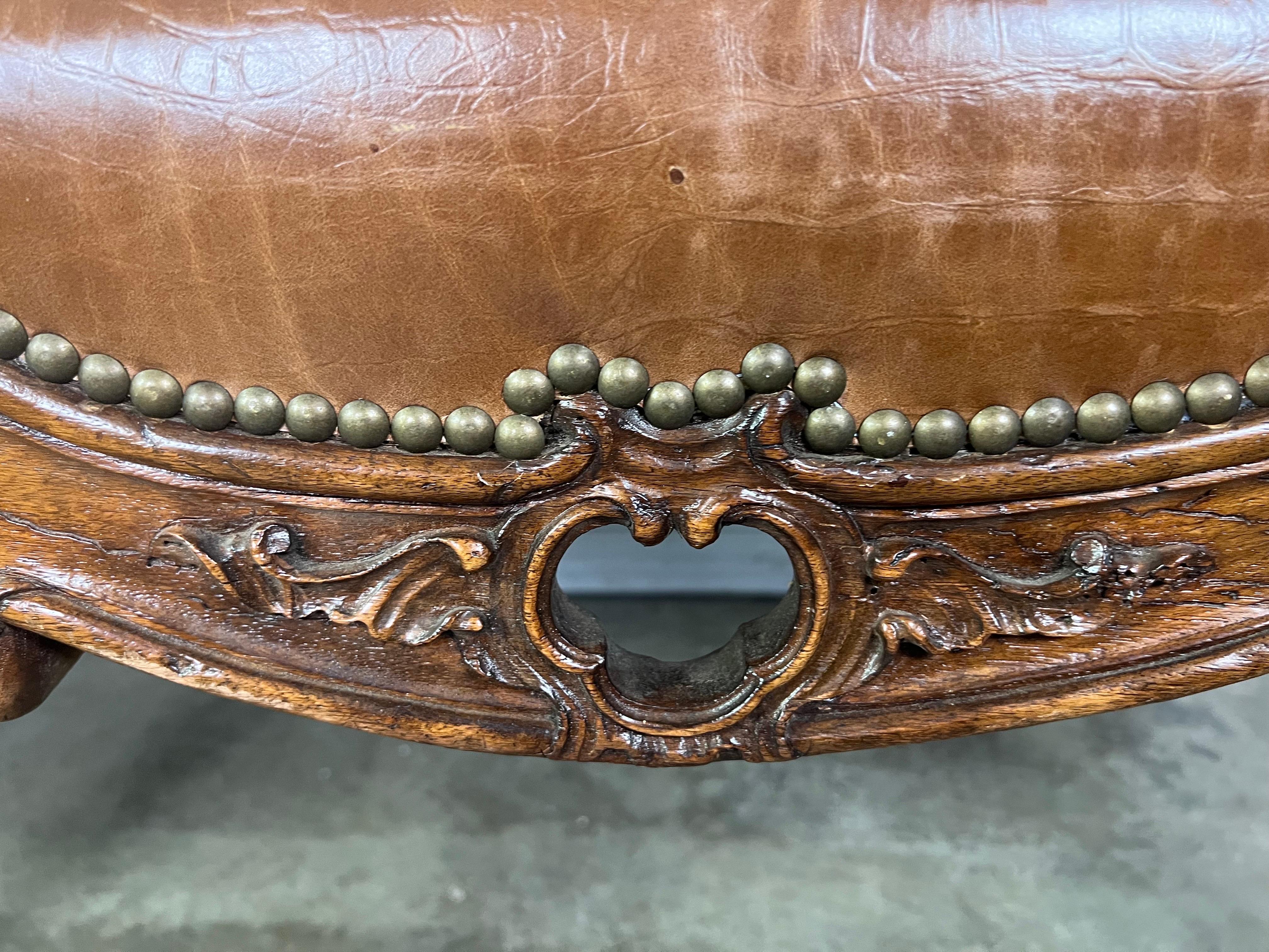 19th century French Provence four legged walnut bench covered in a tobacco colored embossed leather with nailhead trim detail. The walnut carved bench has beautiful lines. The bench sits on four carved cabriole legs. The sides of the bench angle