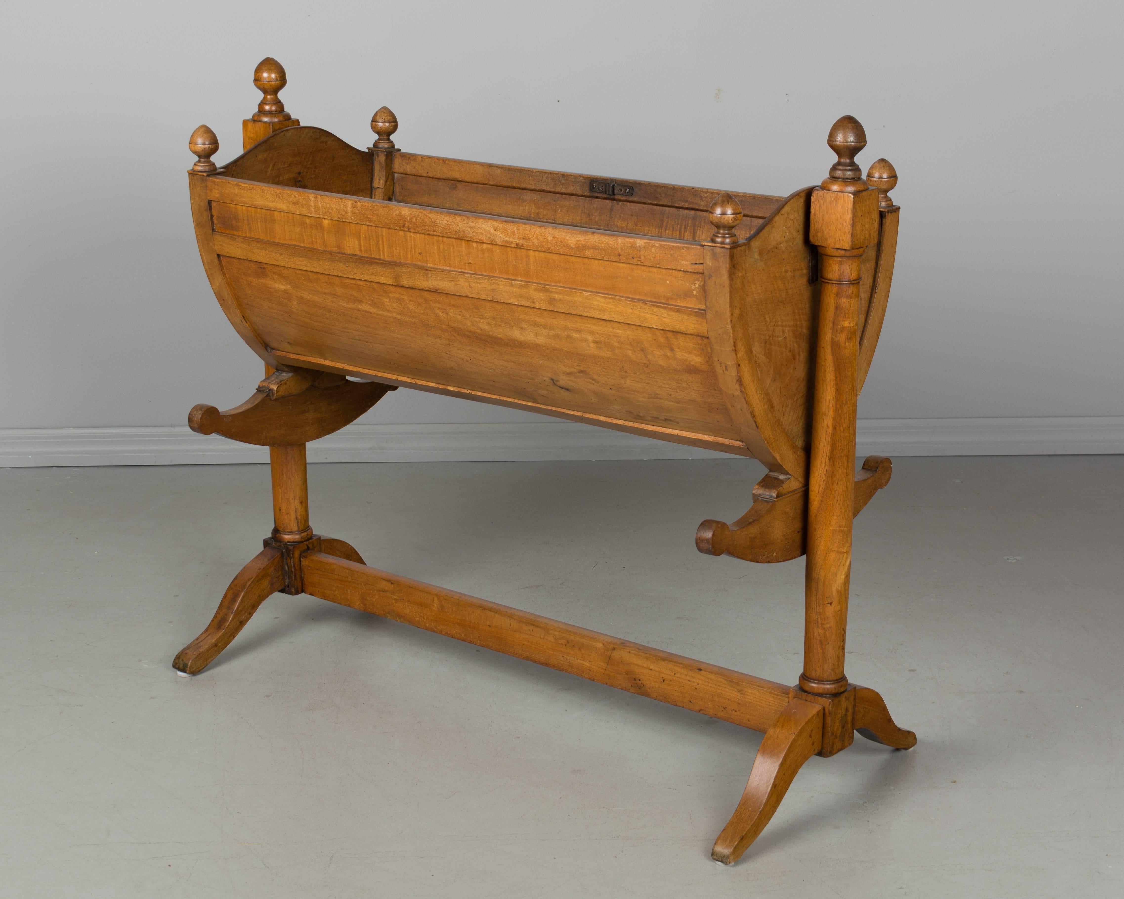 A 19th century French Empire style baby cradle that has been converted to a planter with a newer removable zinc trough. The stand is sturdy and the cradle rocks, but the bottom plank of the bed has been removed. Made of solid walnut with turned