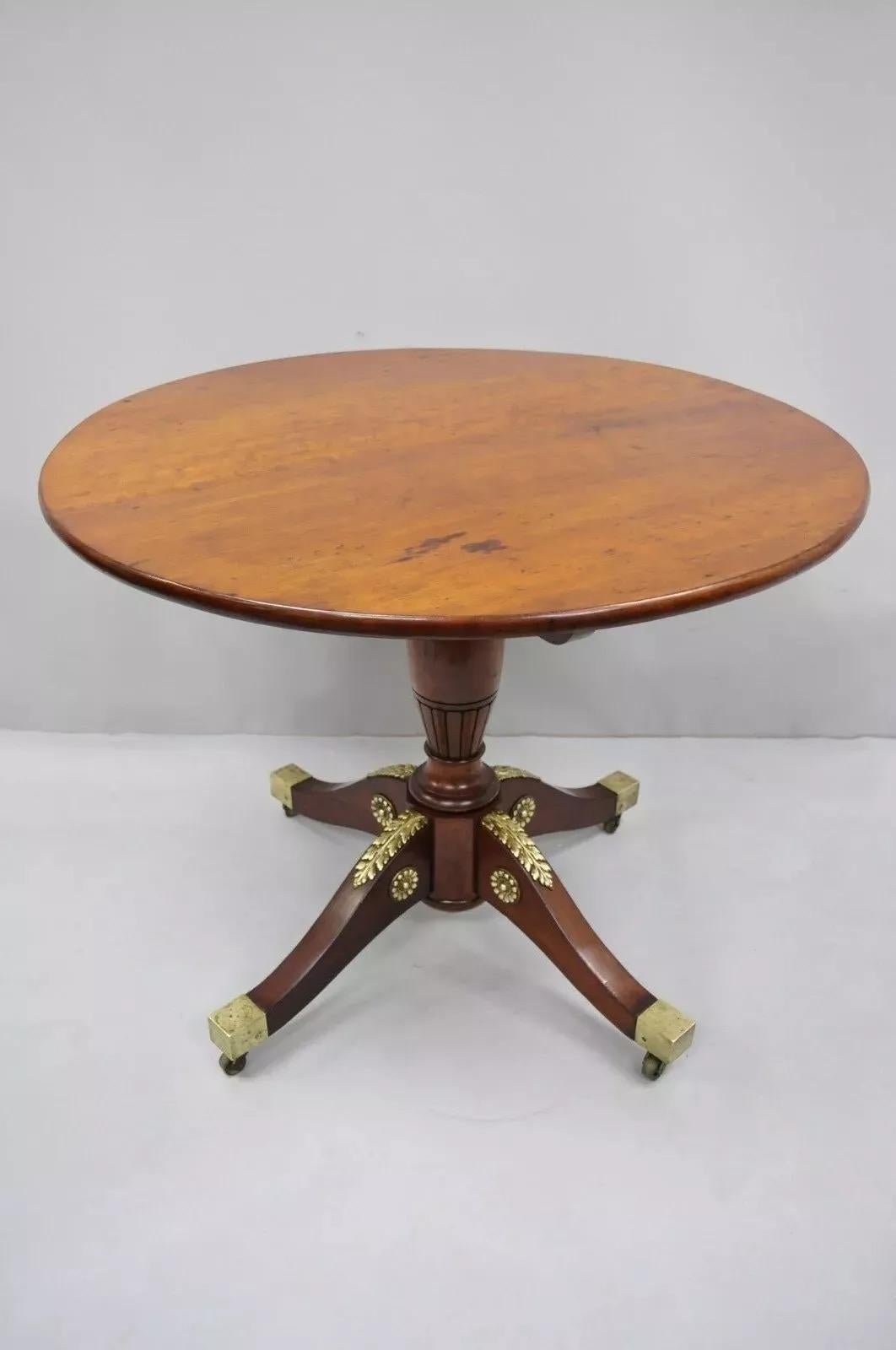 Table ronde à plateau basculant en acajou de style Empire français du 19e siècle, avec ornements en bronze. L'objet présente des ornements en bronze doré, des roulettes en laiton, une colonne centrale sculptée, un beau grain de bois, un très bel