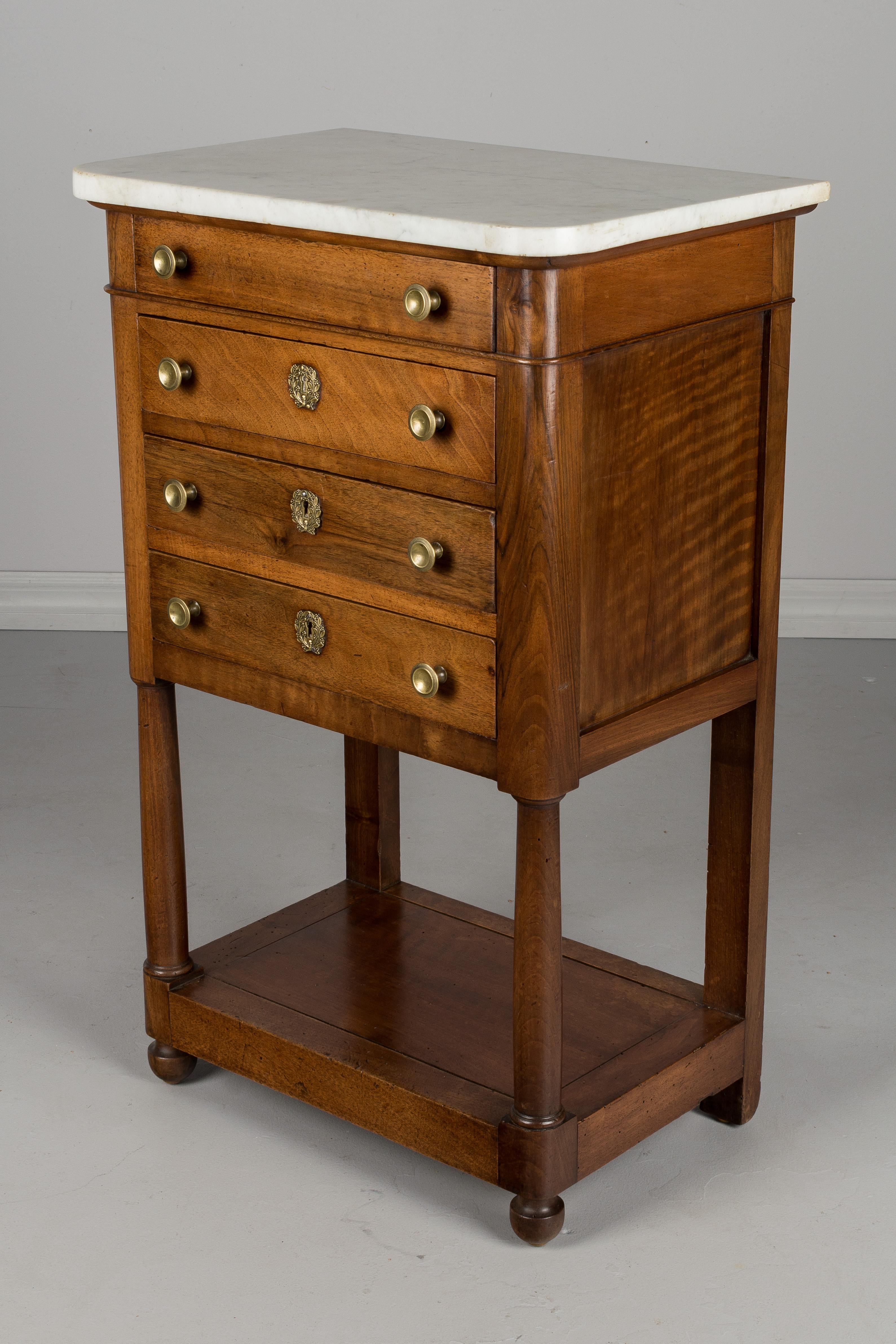 A 19th century French Empire style walnut side table, or nightstand. Four dovetailed drawers with original brass hardware. Two bottom drawers with locks, but no keys. Turned wood columns in the front. White marble top is original and is not