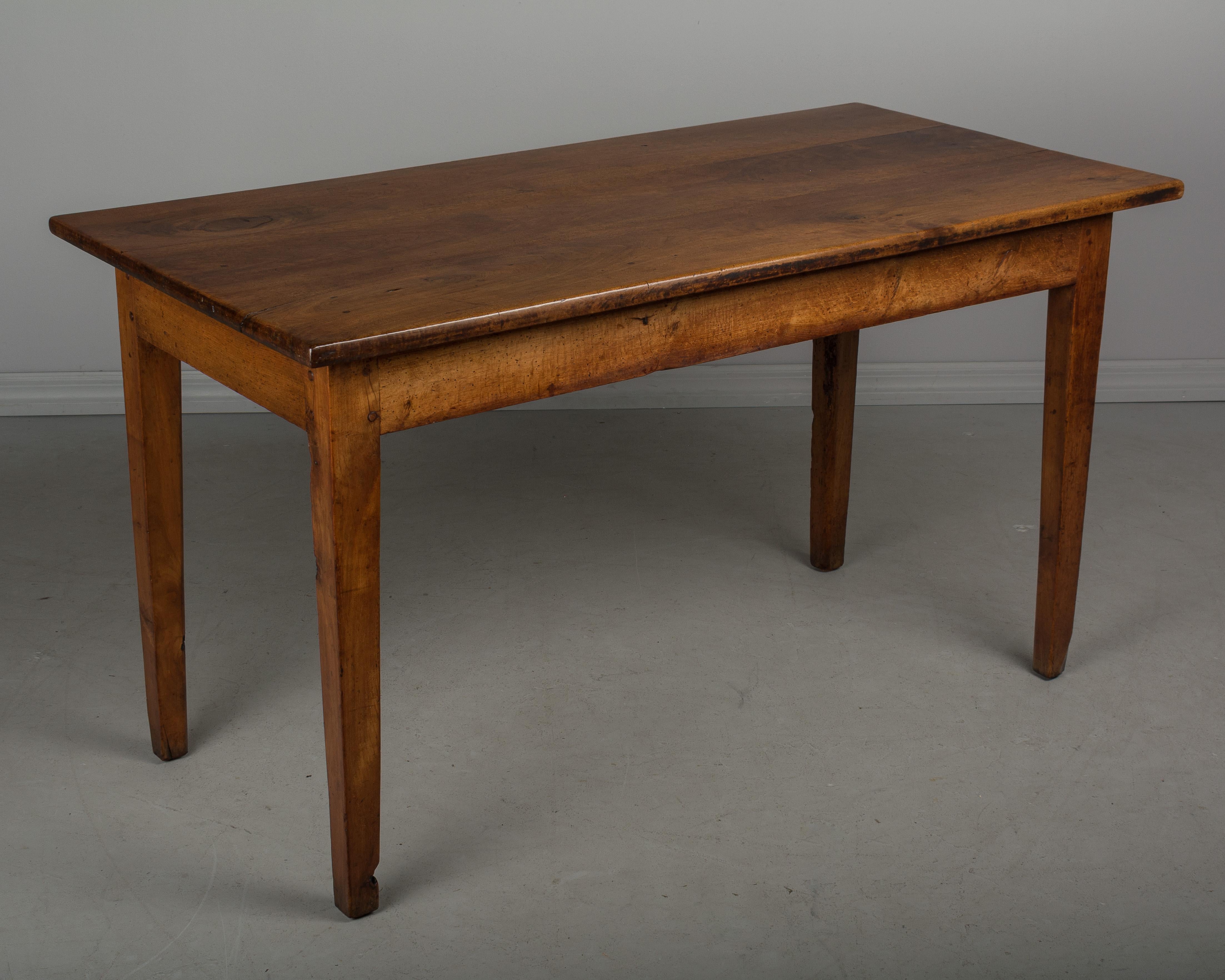 A late 19th century French farm table with a top made of three planks of solid walnut. The base has tapered legs and is made of cherrywood. Sturdy and well made using pegged construction. Small in size, this table was likely used in a kitchen or
