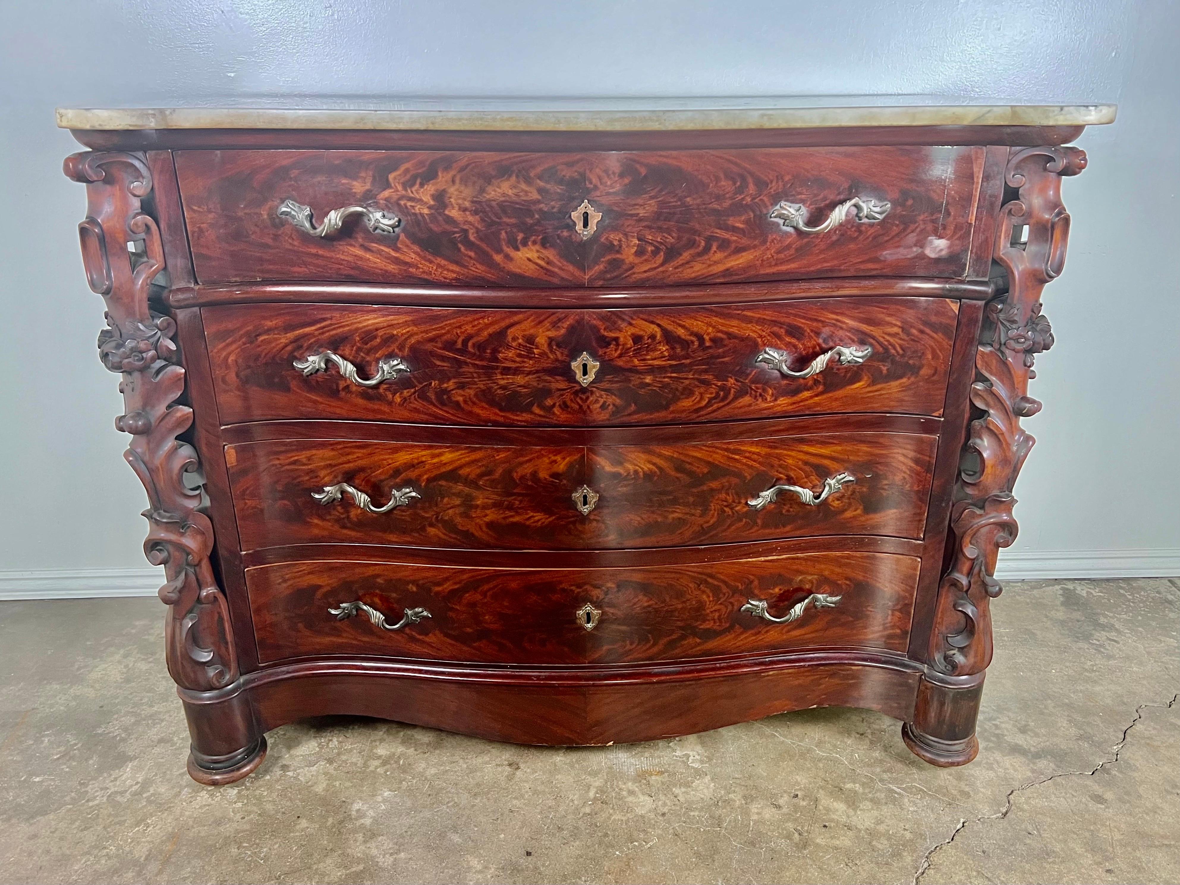 19th century English feathered mahogany chest of drawers. There are finely carved panels flanking the chest that depict leaves, flowers, and acanthus leaves. 
There are four drawer with plenty of storage. The chest stands on four bun  feet. The
