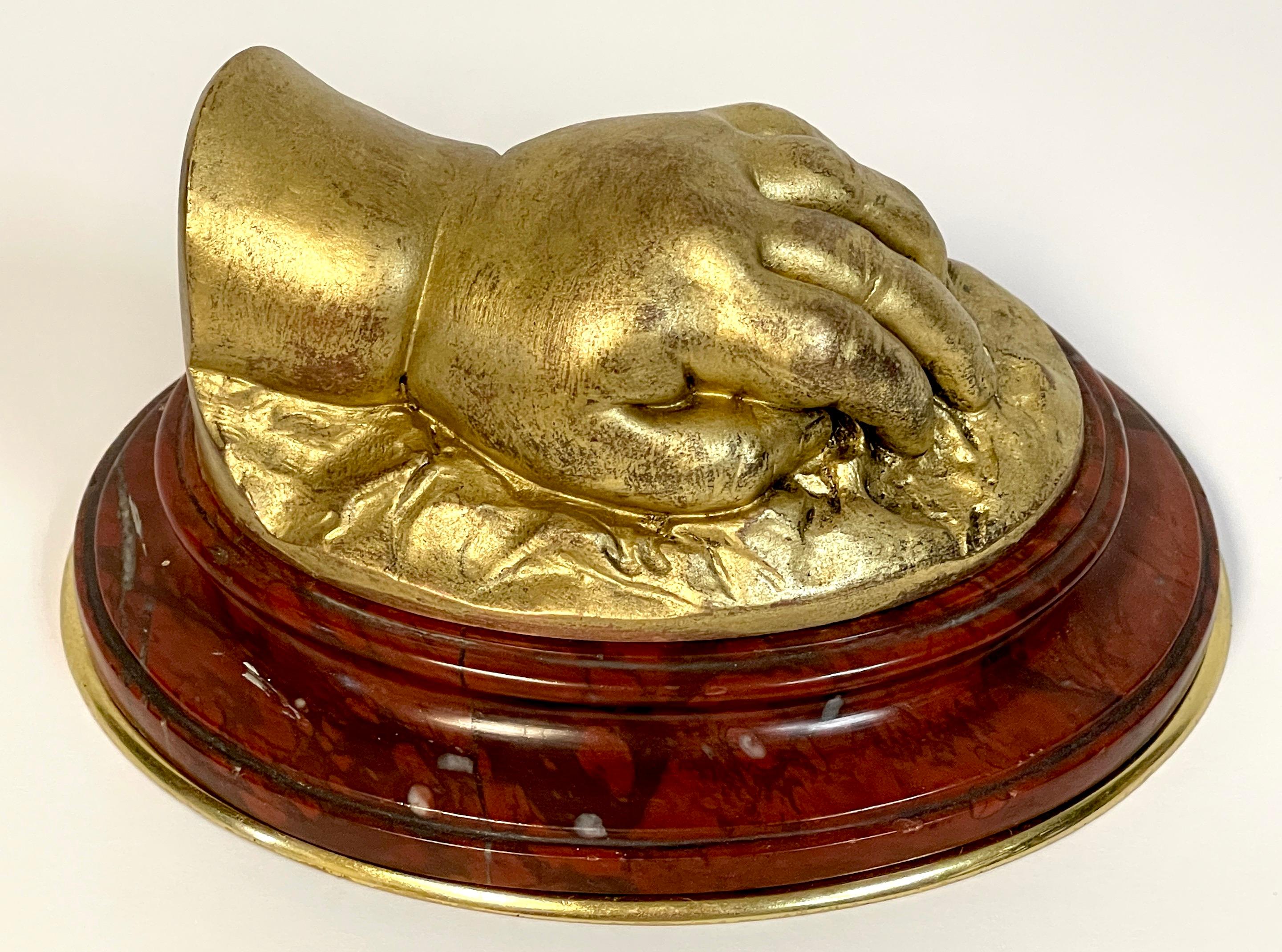 19th century French Gilt Bronze model of a resting hand, Attributed to Barbedienne.
France, Circa 1880s

A unique work, realistically cast model of an ormolu of a resting hand on a draped base, raised on an oval beveled, polished red marble and
