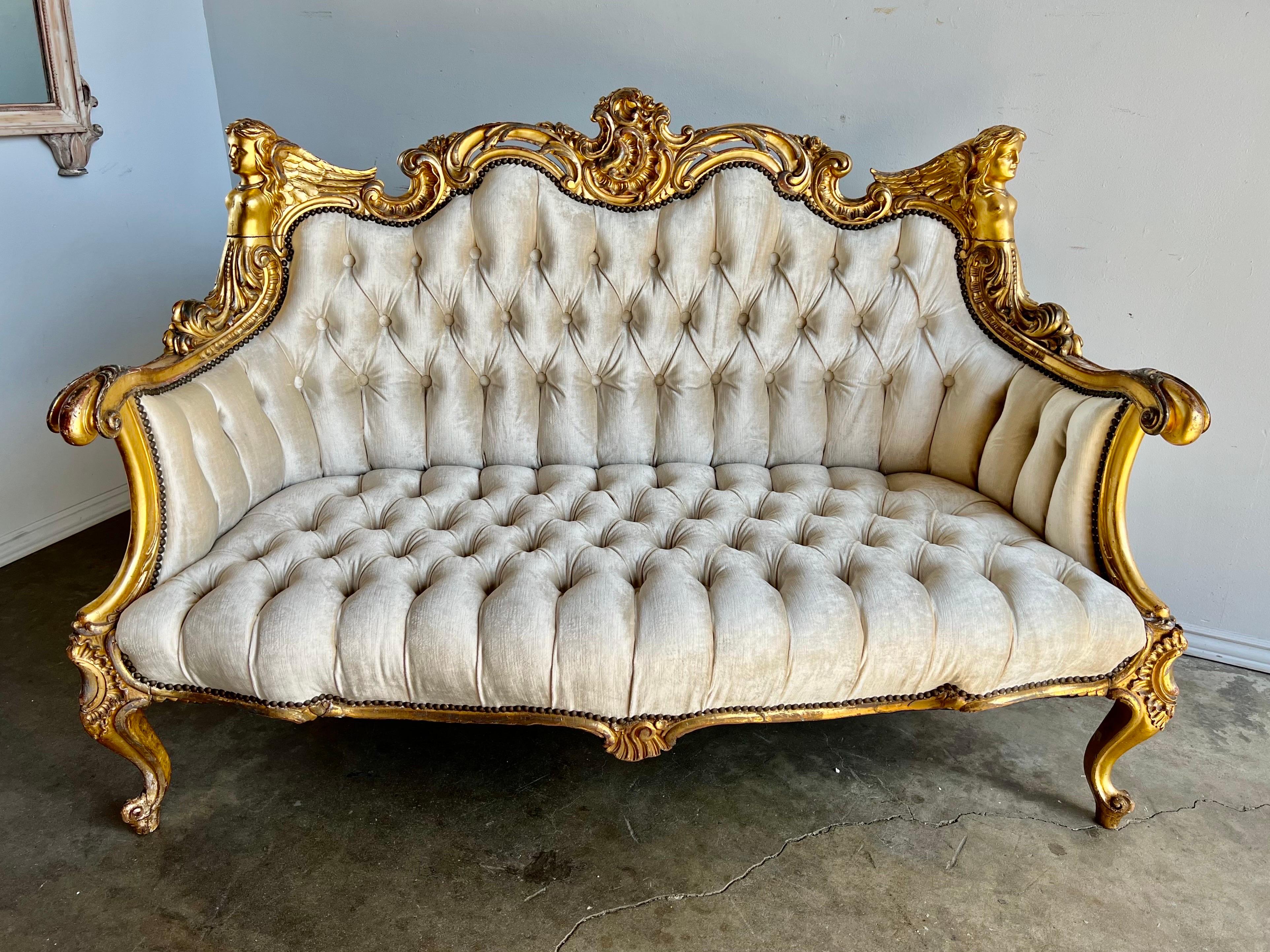 19th Century French Louis XiV style gilt wood settee depicting carved wood angels, flowers, cartouches, acanthus leaves and more. The settee is newly upholstered in a cream velvet with nailhead trim.