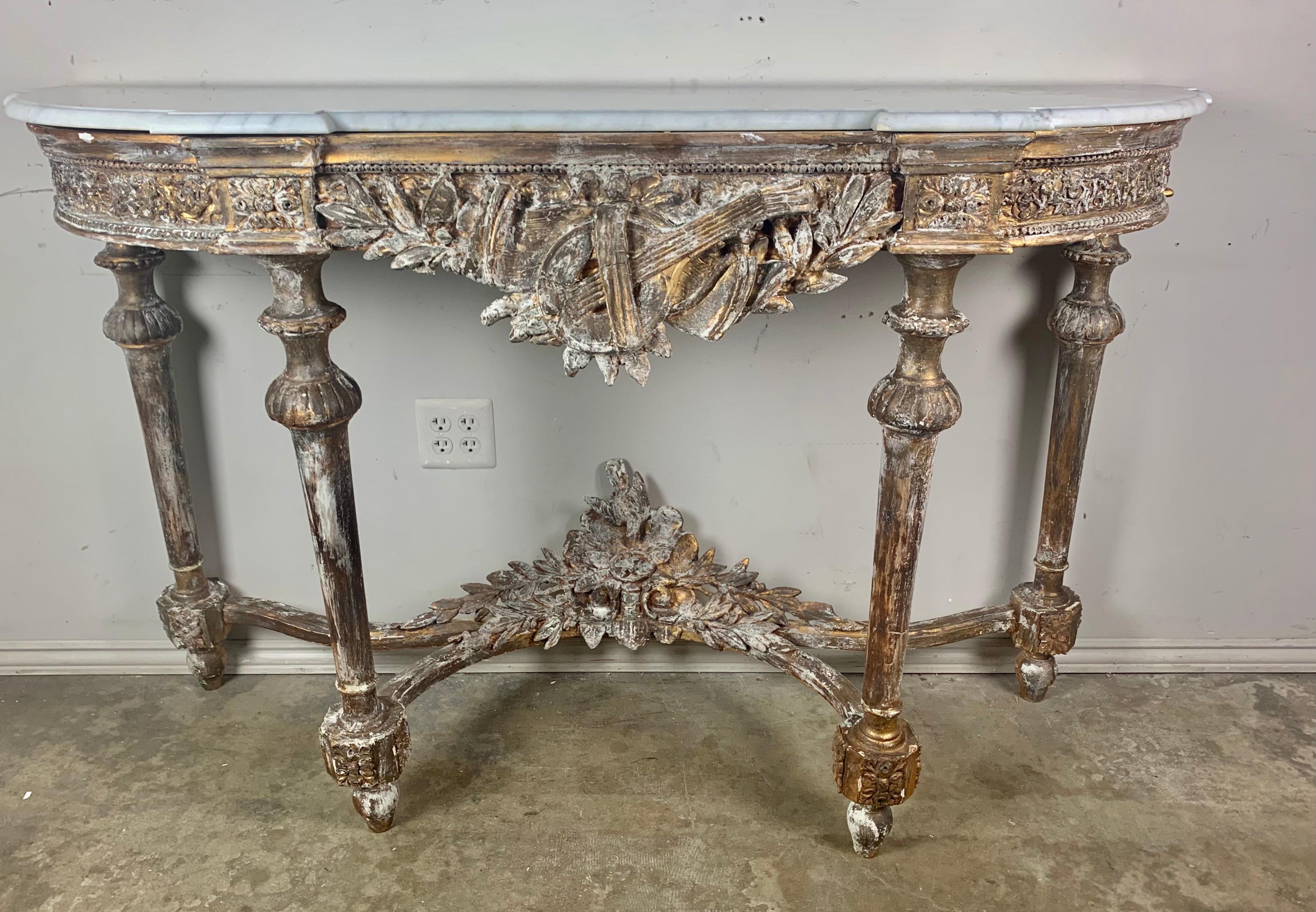 19th C. French gilt wood Louis XVI style console with Carrara marble top. The console stands on four straights legs that meet at a carved stretcher with intricate details throughout. The apron of the console depicts an instrument, laurel leaves,