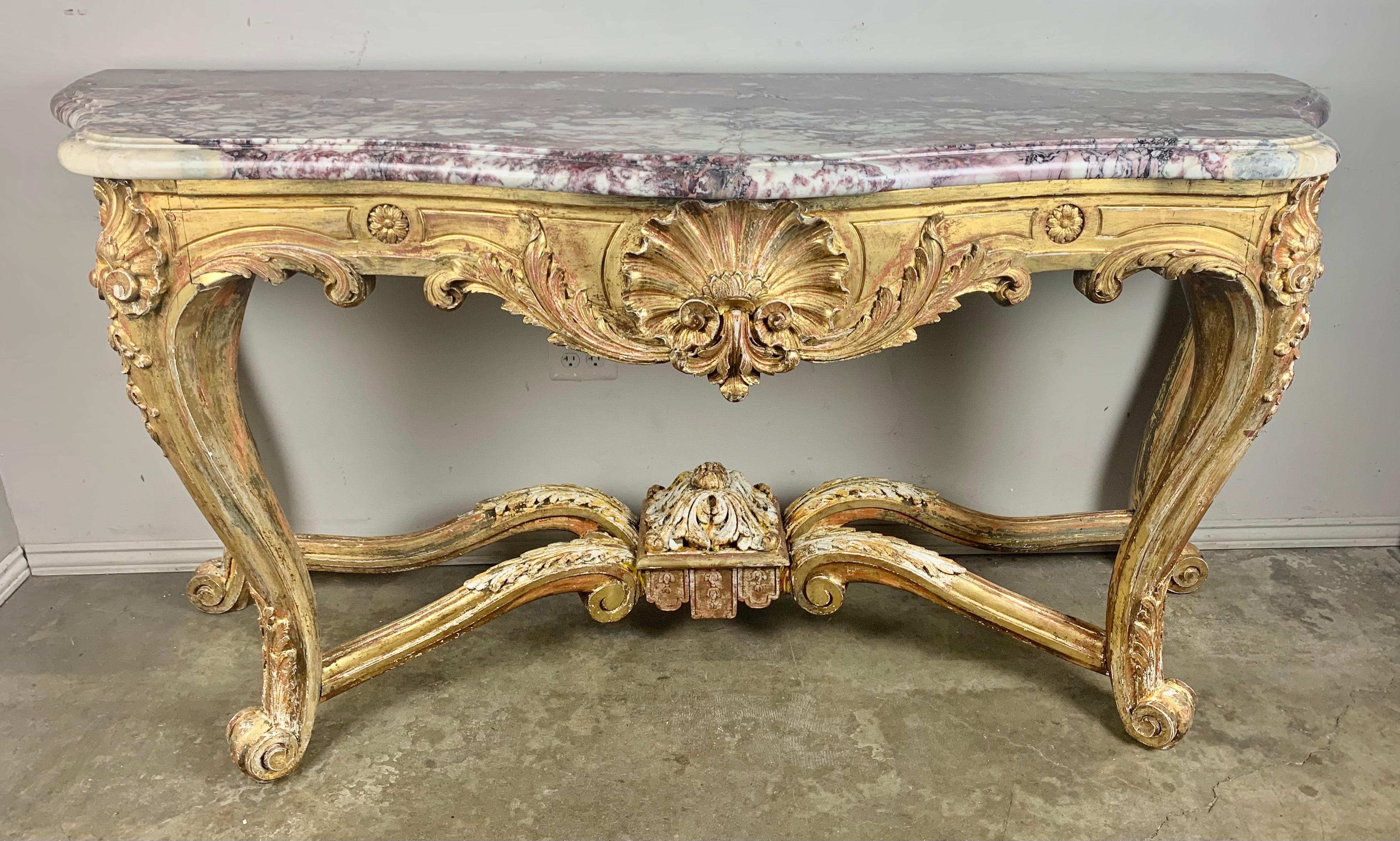 19th C. French giltwood Rococo style console with original marble top. The monumental piece stands on four cabriole legs that connect to a bottom stretcher. The console has carving throughout depicting a center shell motif flanked by a pair of