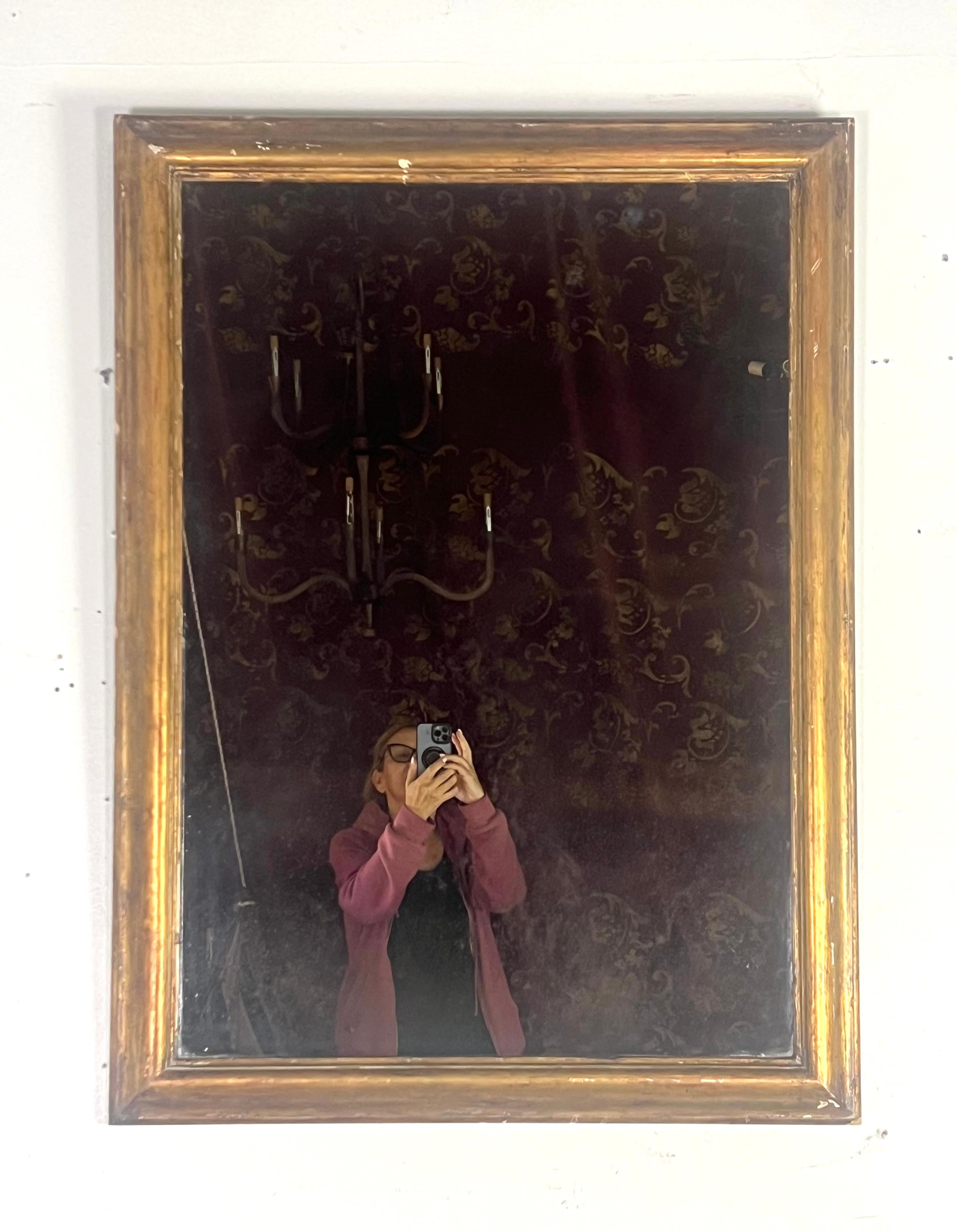 19th century giltwood mirror with a rectangular shape and a simple yet elegant frame.  The frame is finished in a warm. gold leaf finish with a slightly distressed look, showing some signs of age and wear.  The frame has a smooth surface with no