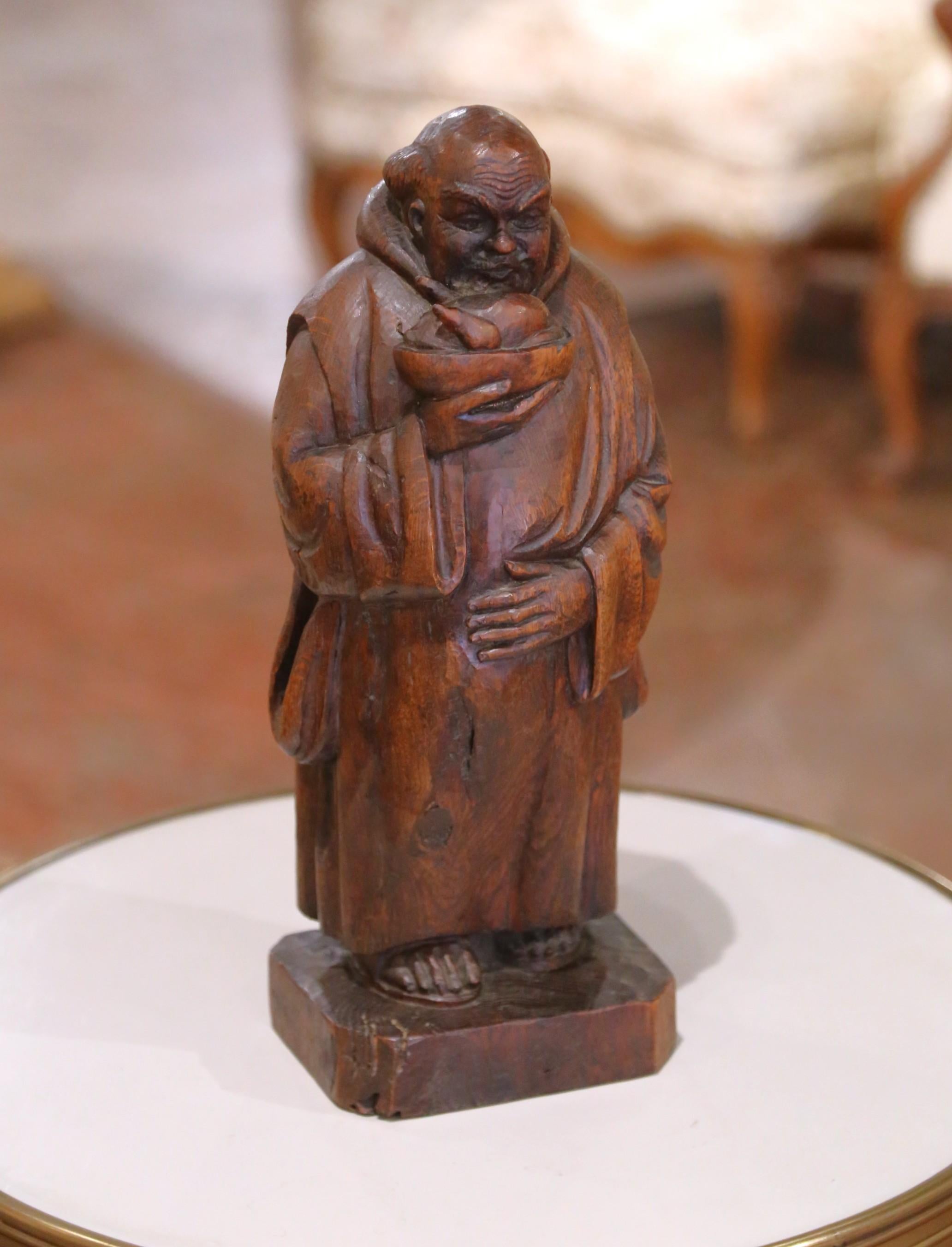 Hand-carved in France circa 1880, this evocative oak figure depicts a solemn hooded monk cradling a bowl, likely a symbol of humility, almsgiving, or simple monastic life. Sculpted from solid oak with rich grain and deep patina, the figure wears a