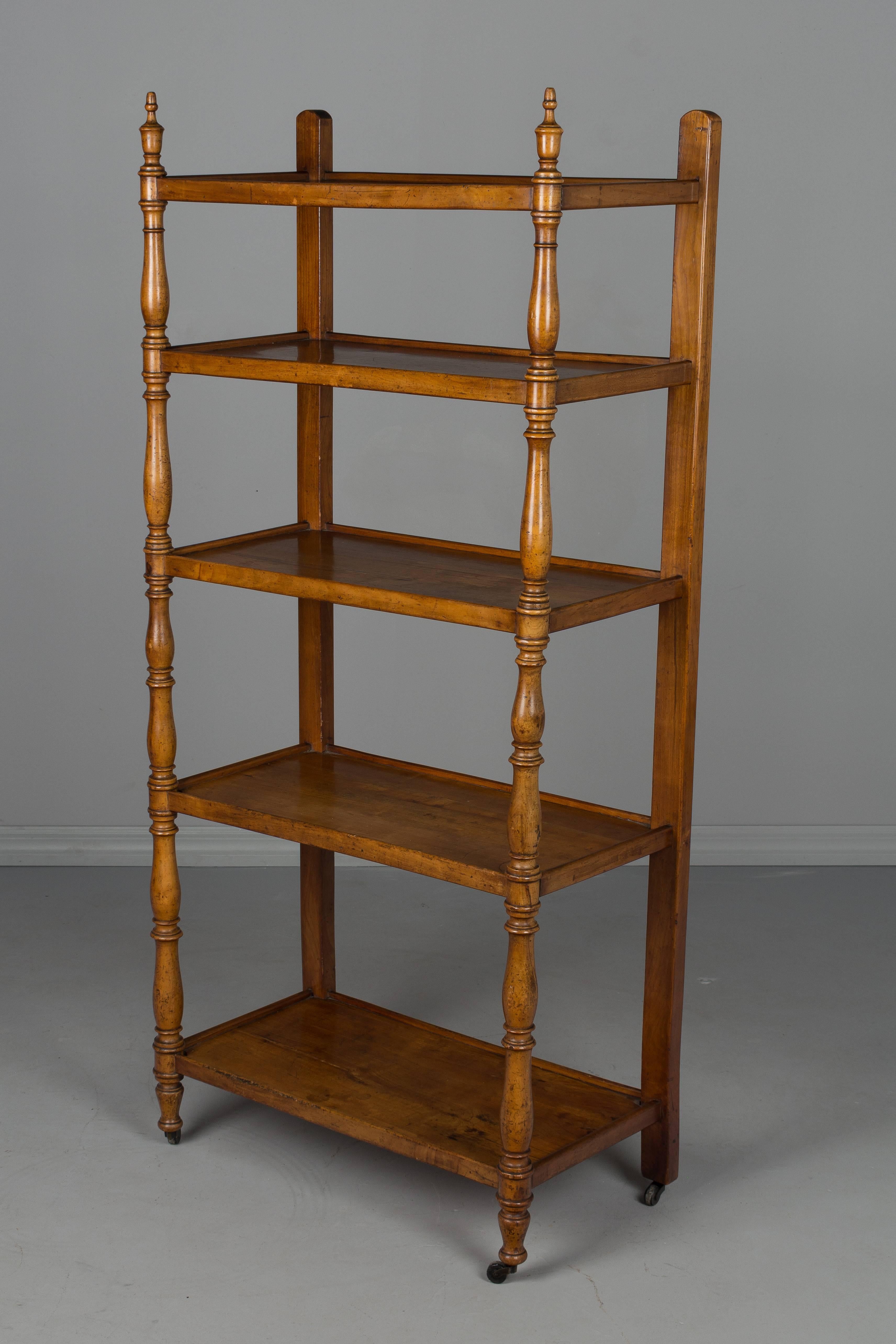 A 19th century French Louis Philippe etagere, or book shelf, made of solid cheerywood. Turned front posts with finials. Original wheels. In good condition with normal wear. Sturdy, but leans slightly to the right depending where the wheels are.